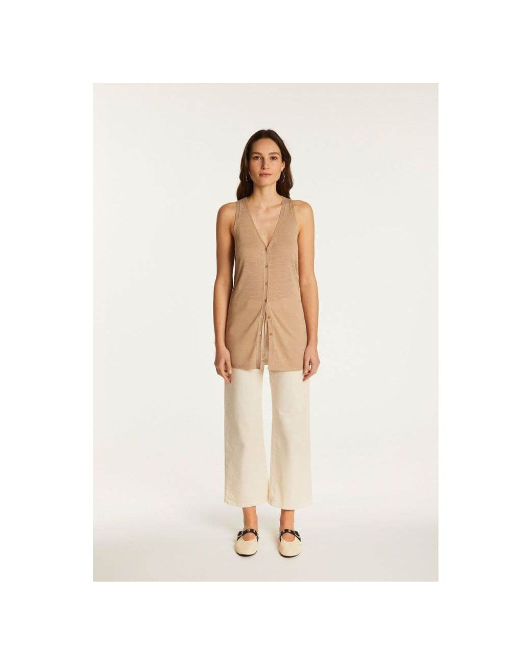 Woman wearing a lightweight linen short-sleeve vest top styled with white trousers for a chic summer look.