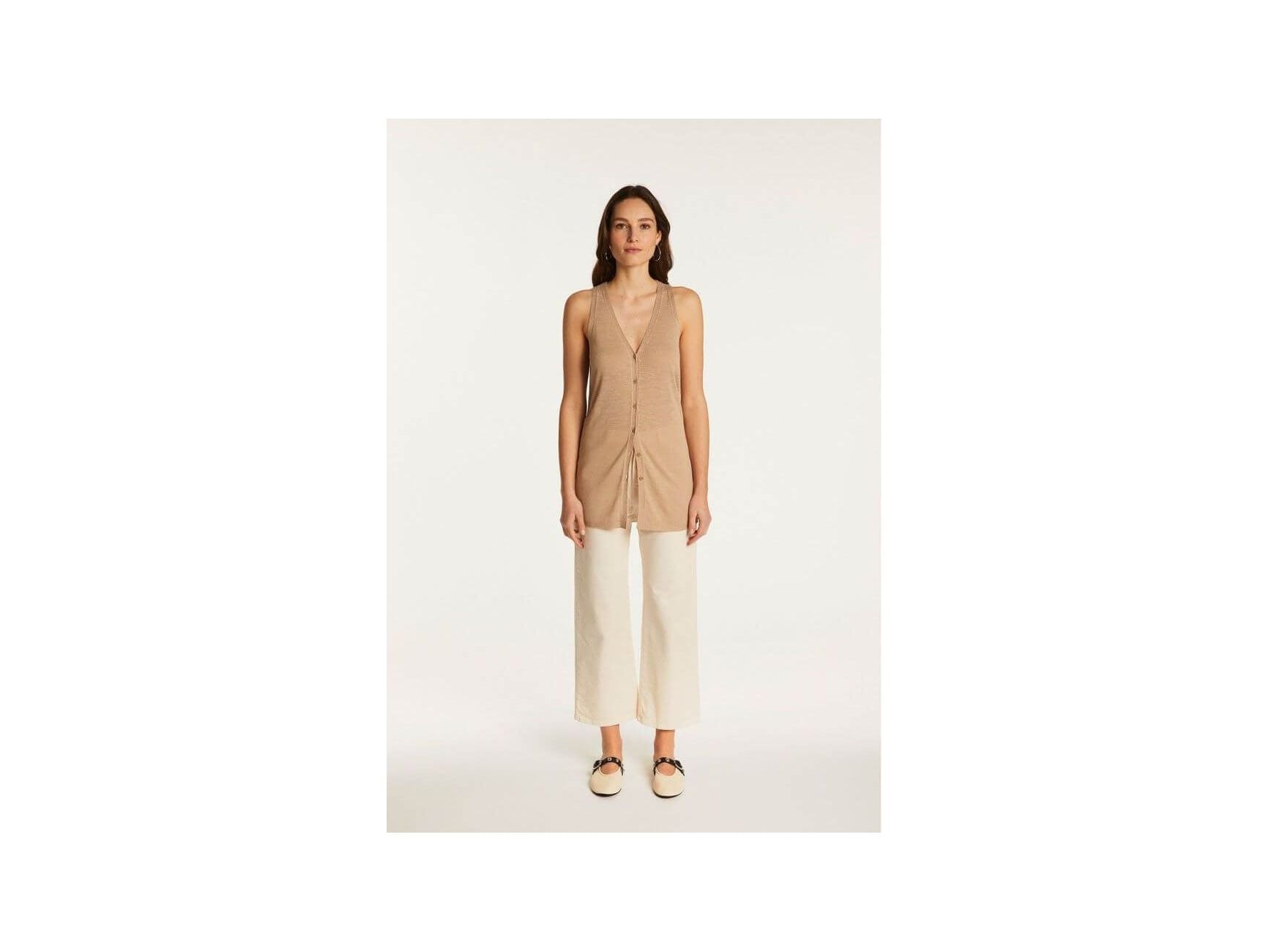 Woman wearing a lightweight linen short-sleeve vest top styled with white trousers for a chic summer look.