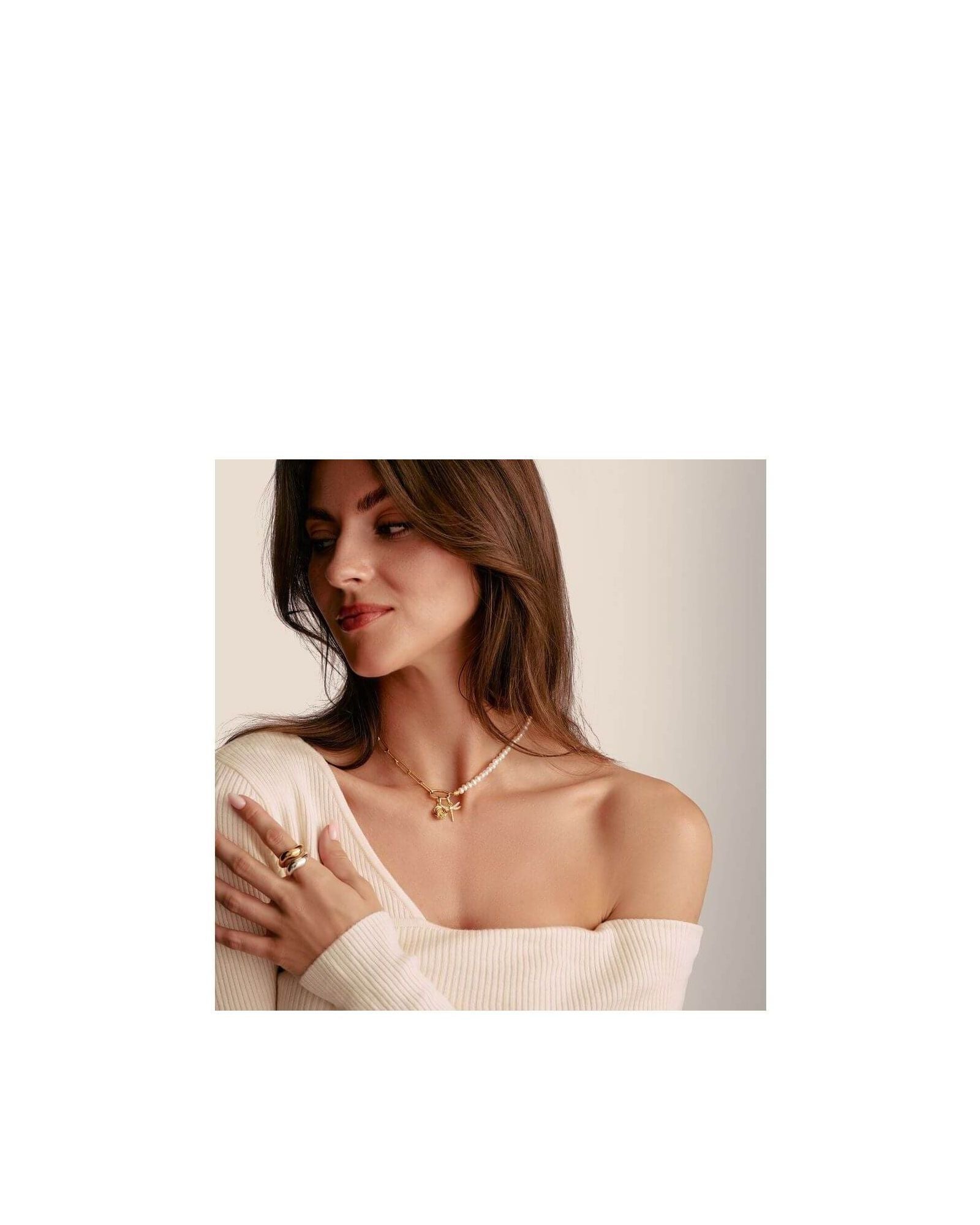 Femme portant un pendentif charm fleur de rose en plaqué or, avec un pull ample et des bijoux assortis.
