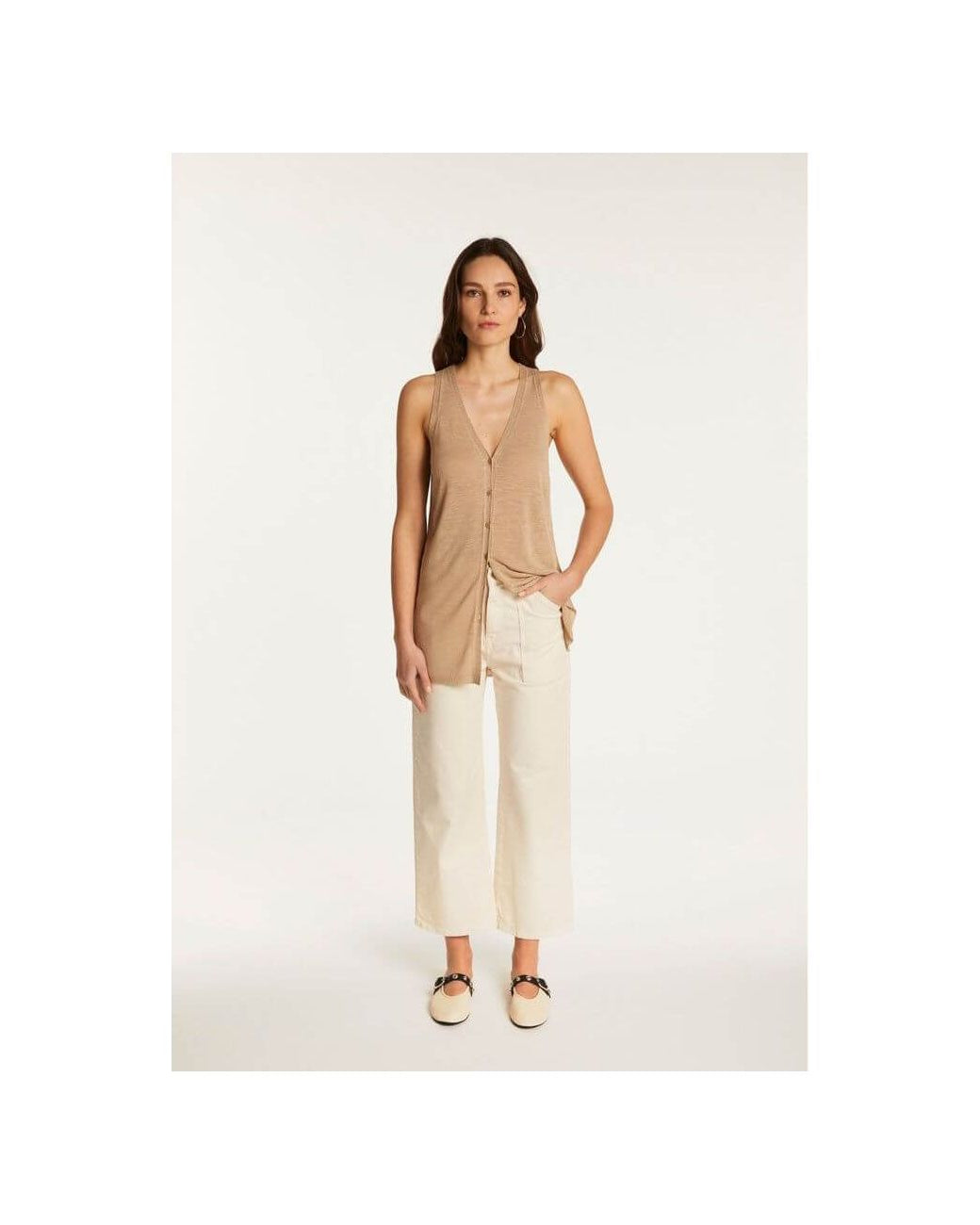 Femme portant un gilet léger à manches courtes en lin flammé, associé à un pantalon blanc, look estival chic.