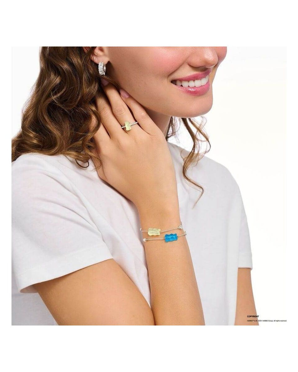 Femme portant un bracelet en argent avec ours d'or bleu et perle, affichant un sourire et des bijoux délicats.