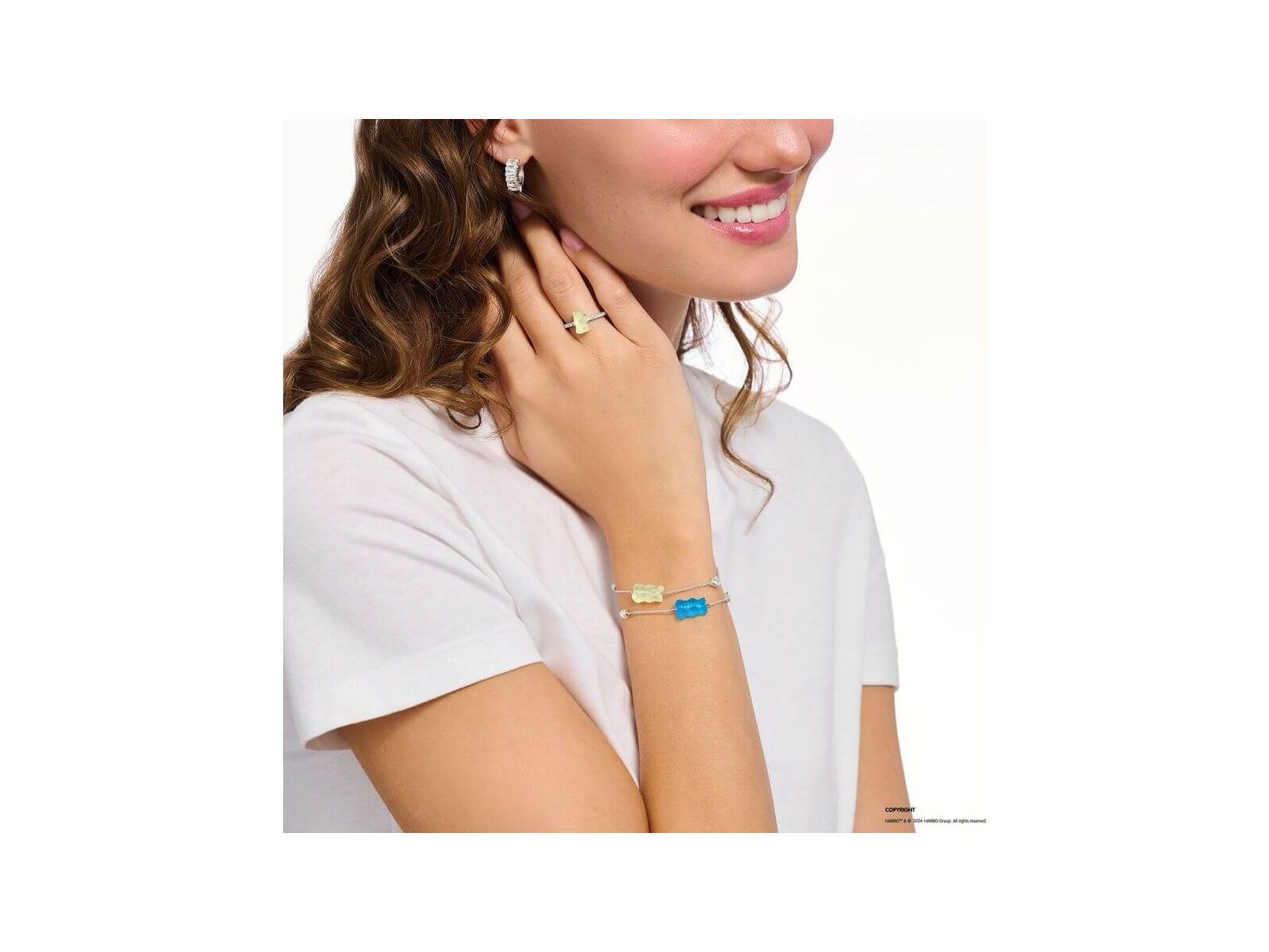 Femme portant un bracelet en argent avec ours d'or bleu et perle, affichant un sourire et des bijoux délicats.