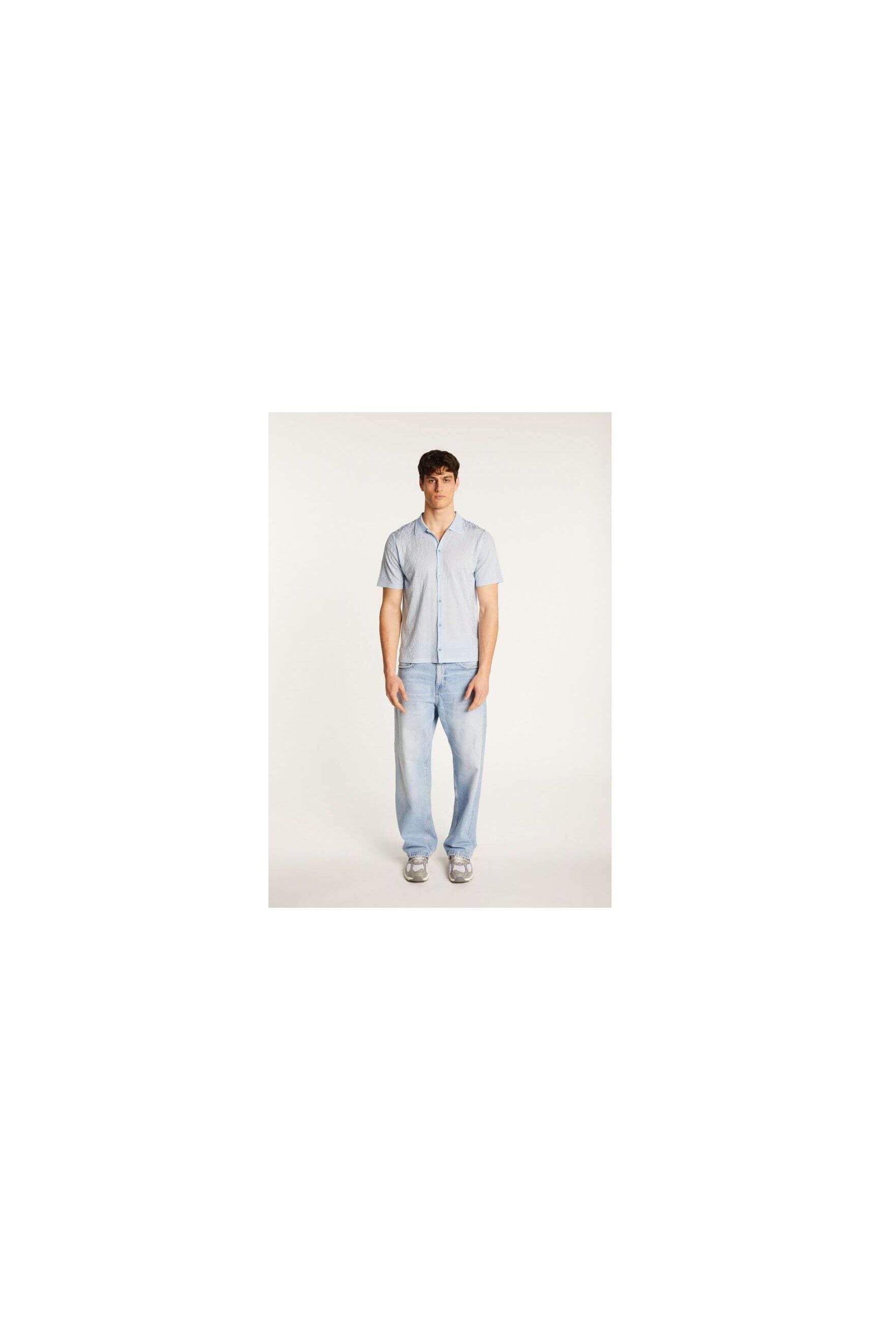 Model wearing the Matthew short-sleeve shirt in blue, paired with light jeans for a casual summer look.