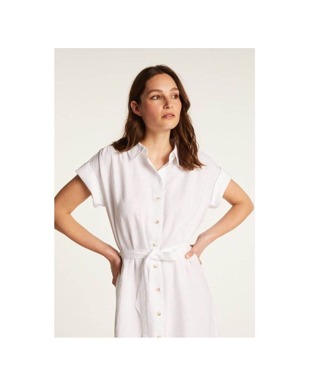 Femme portant une robe blanche Emy en lin léger, dotée de boutons et d'une ceinture pour un look élégant.