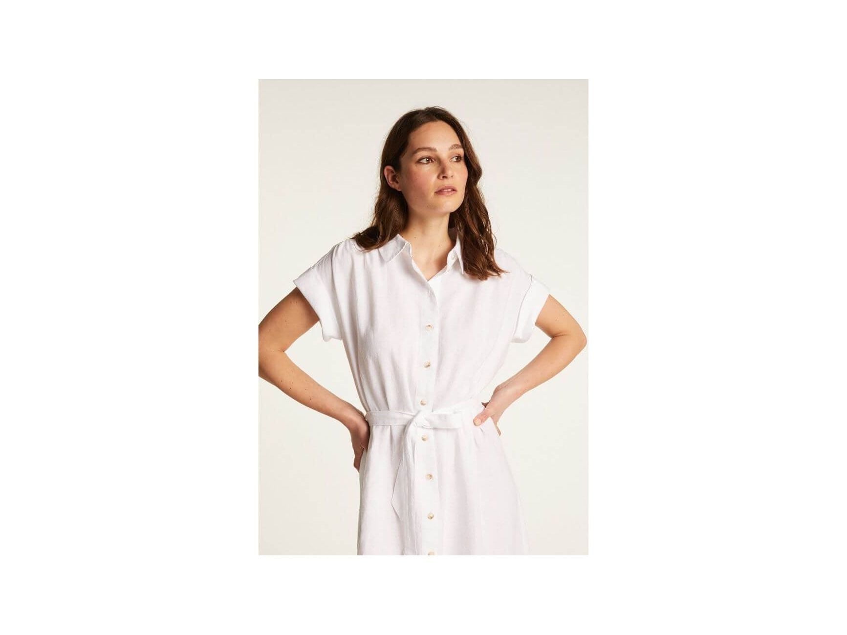 Femme portant une robe blanche Emy en lin léger, dotée de boutons et d'une ceinture pour un look élégant.