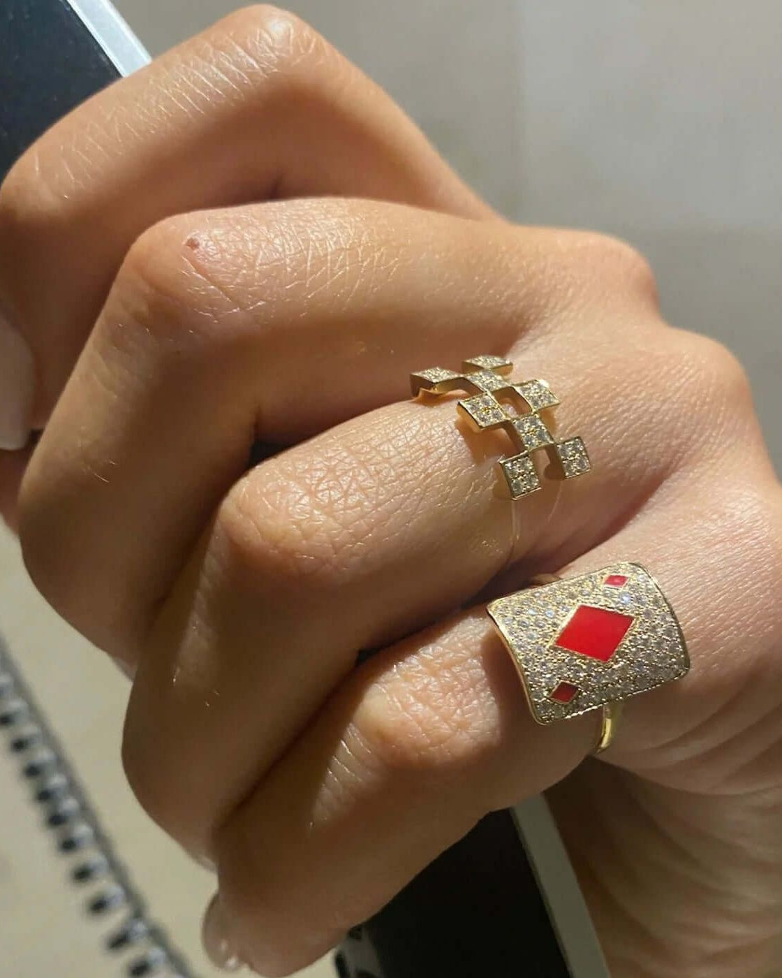 Elegant gold rings adorned with diamonds and red accents, showcasing a stylish hand.