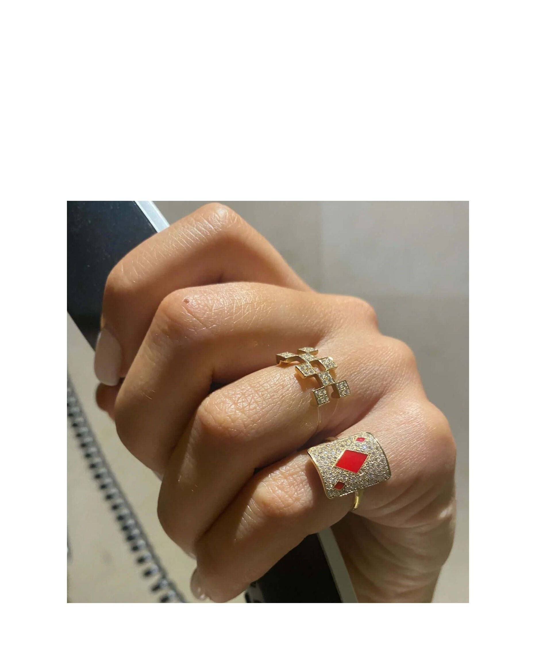 Elegant gold rings adorned with diamonds and red accents, showcasing a stylish hand.