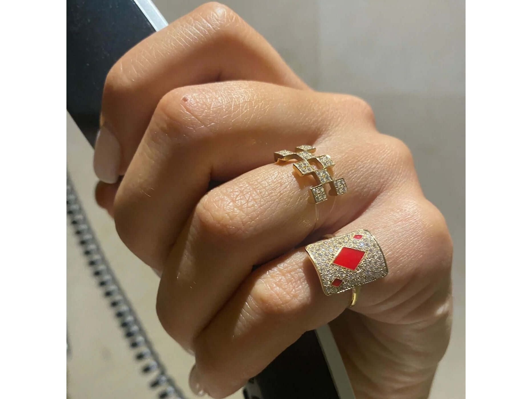 Elegant gold rings adorned with diamonds and red accents, showcasing a stylish hand.