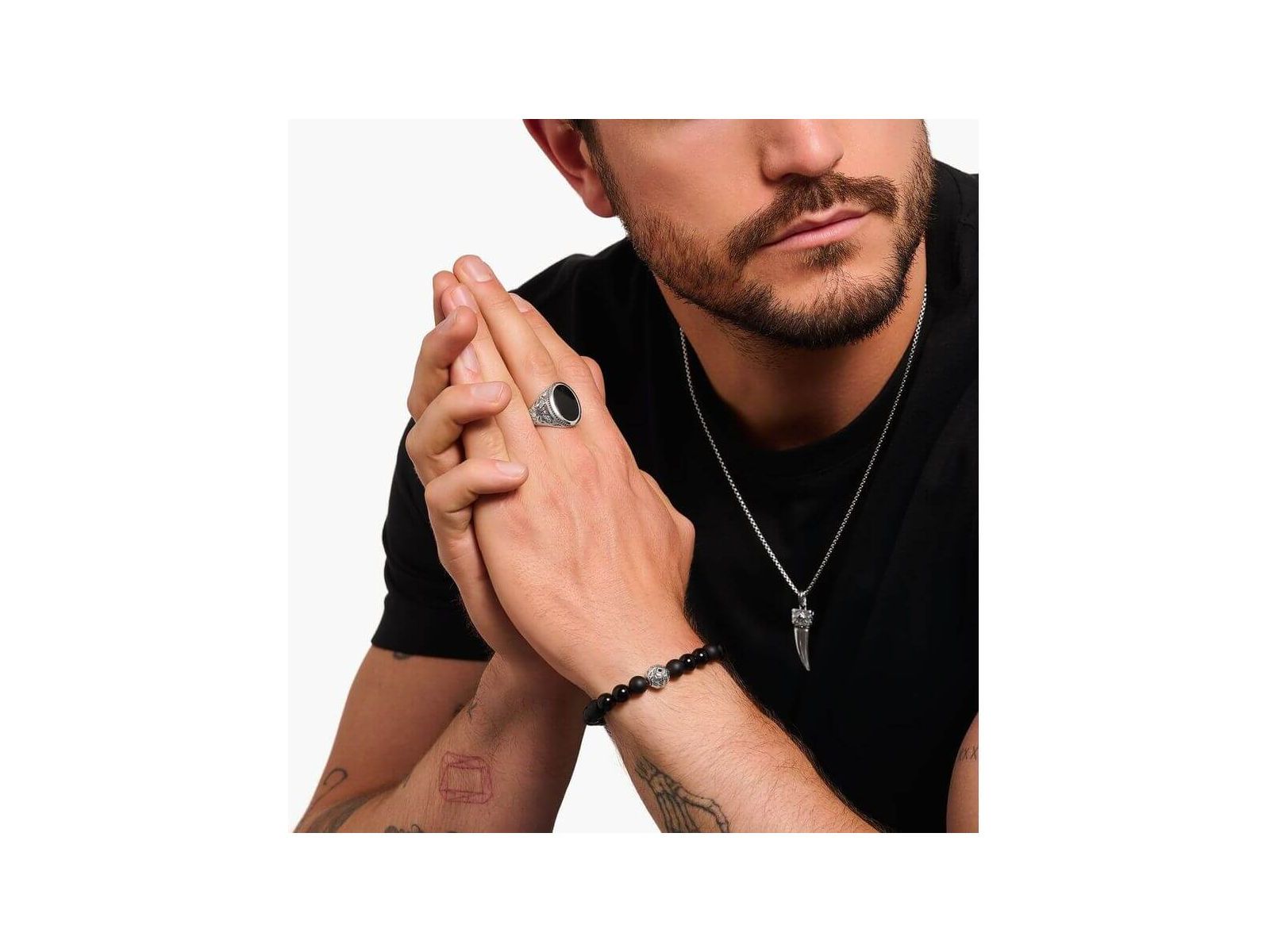 Homme portant une chevalière en argent noirci avec onyx noir, bracelet noir et collier stylé.