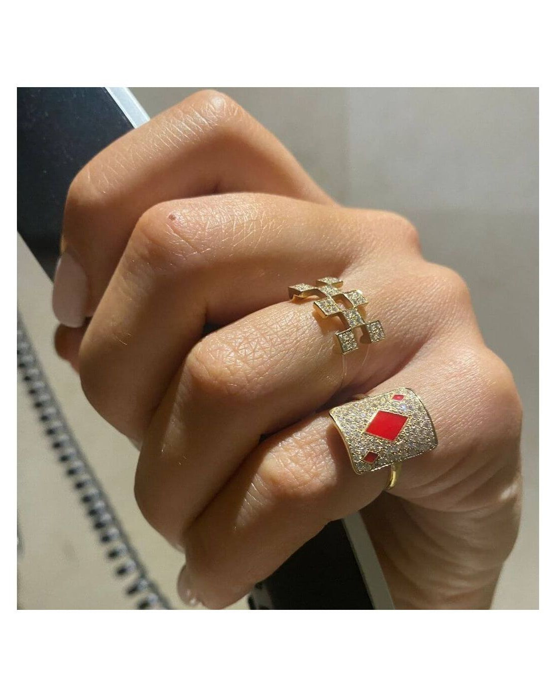 Close-up of a hand wearing two elegant rings, one gold with diamonds and the other with a red gemstone.