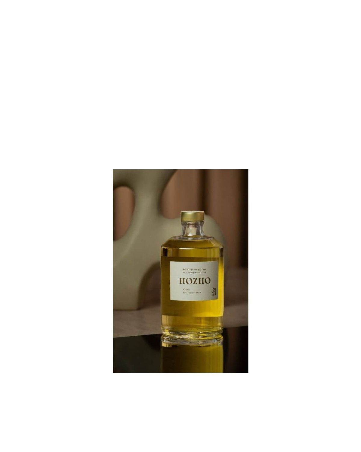 Bouteille d'huile Hozho sur une surface réfléchissante avec fond artistique, mettant en avant une présentation raffinée.