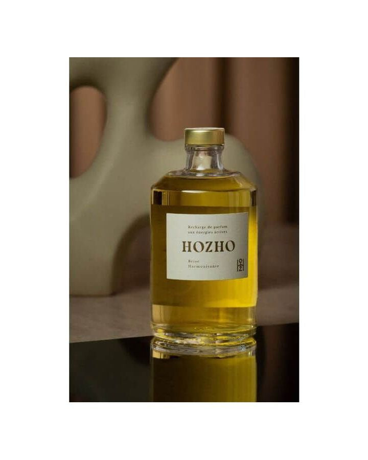 Bouteille d'huile Hozho sur une surface réfléchissante avec fond artistique, mettant en avant une présentation raffinée.
