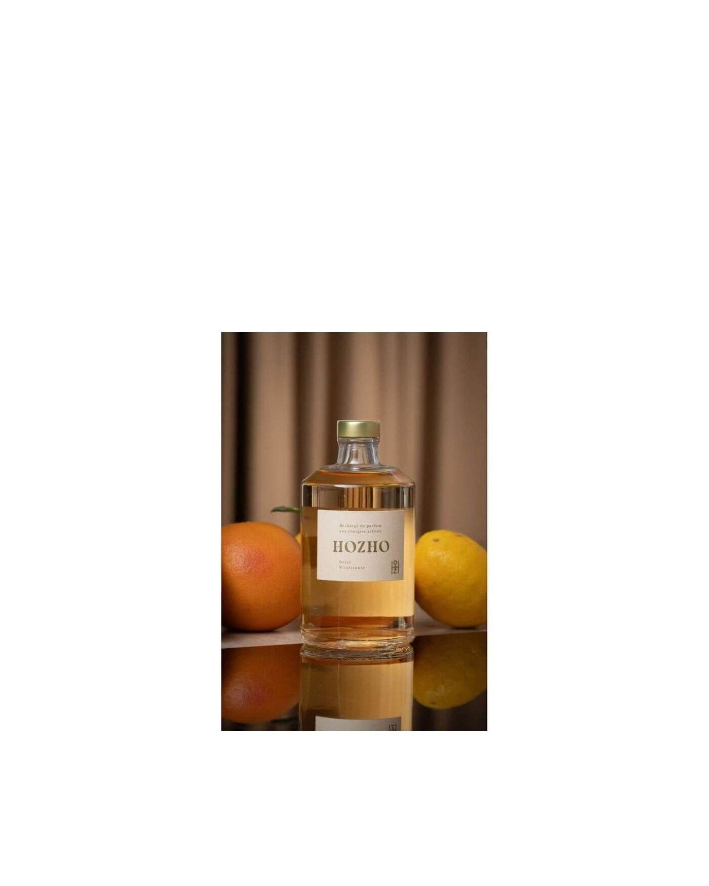 Bouteille de diffuseur HOZHO entourée d'orange et de citron, évoquant une atmosphère revitalisante.
