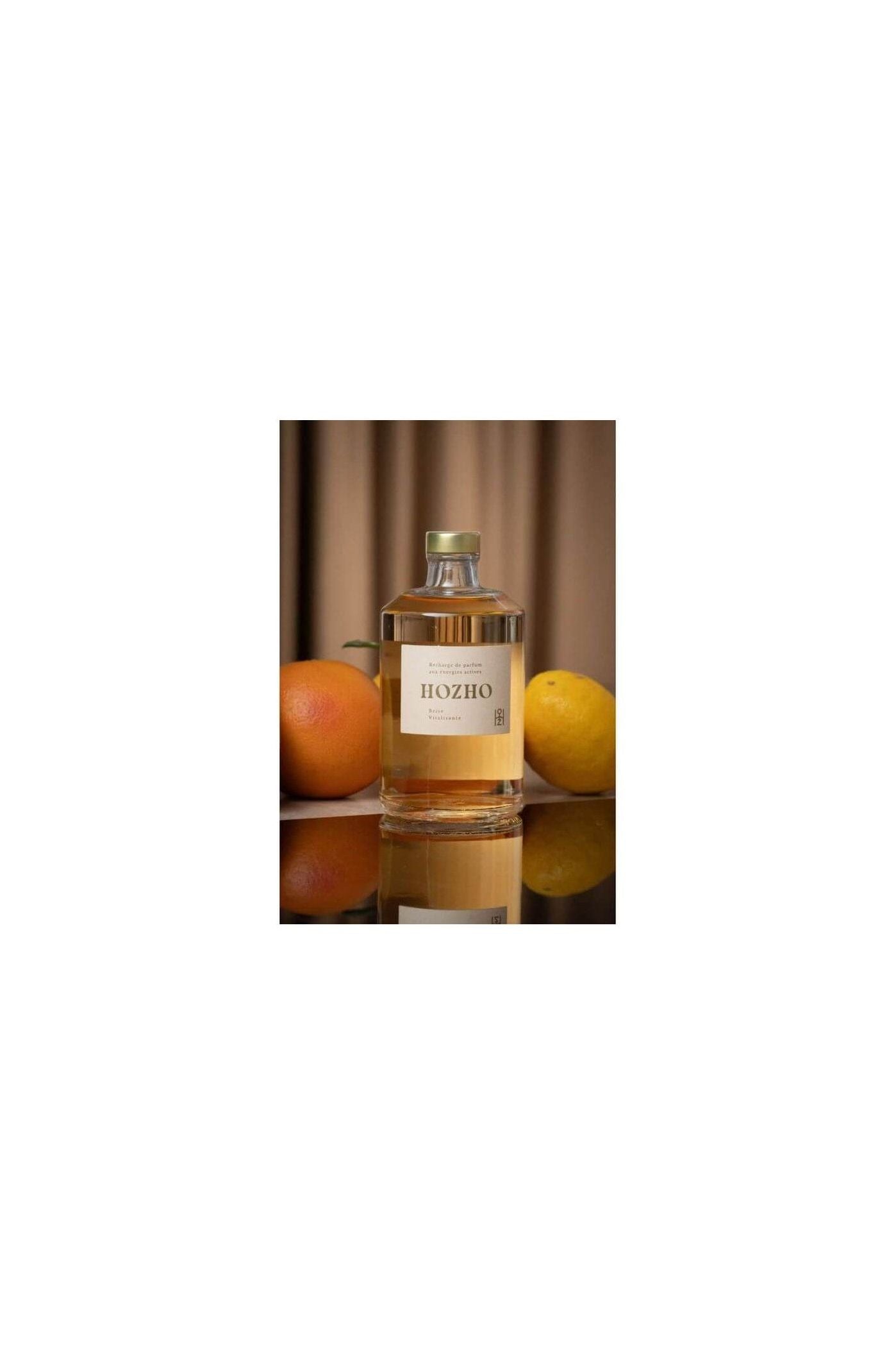 Bouteille de diffuseur HOZHO entourée d'orange et de citron, évoquant une atmosphère revitalisante.