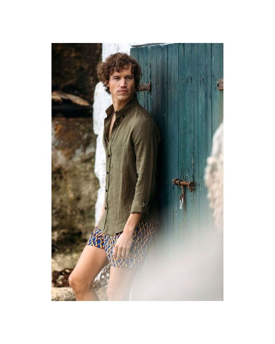 Homme portant une chemise en lin kaki, debout près d'une porte bleue, affichant un style décontracté.