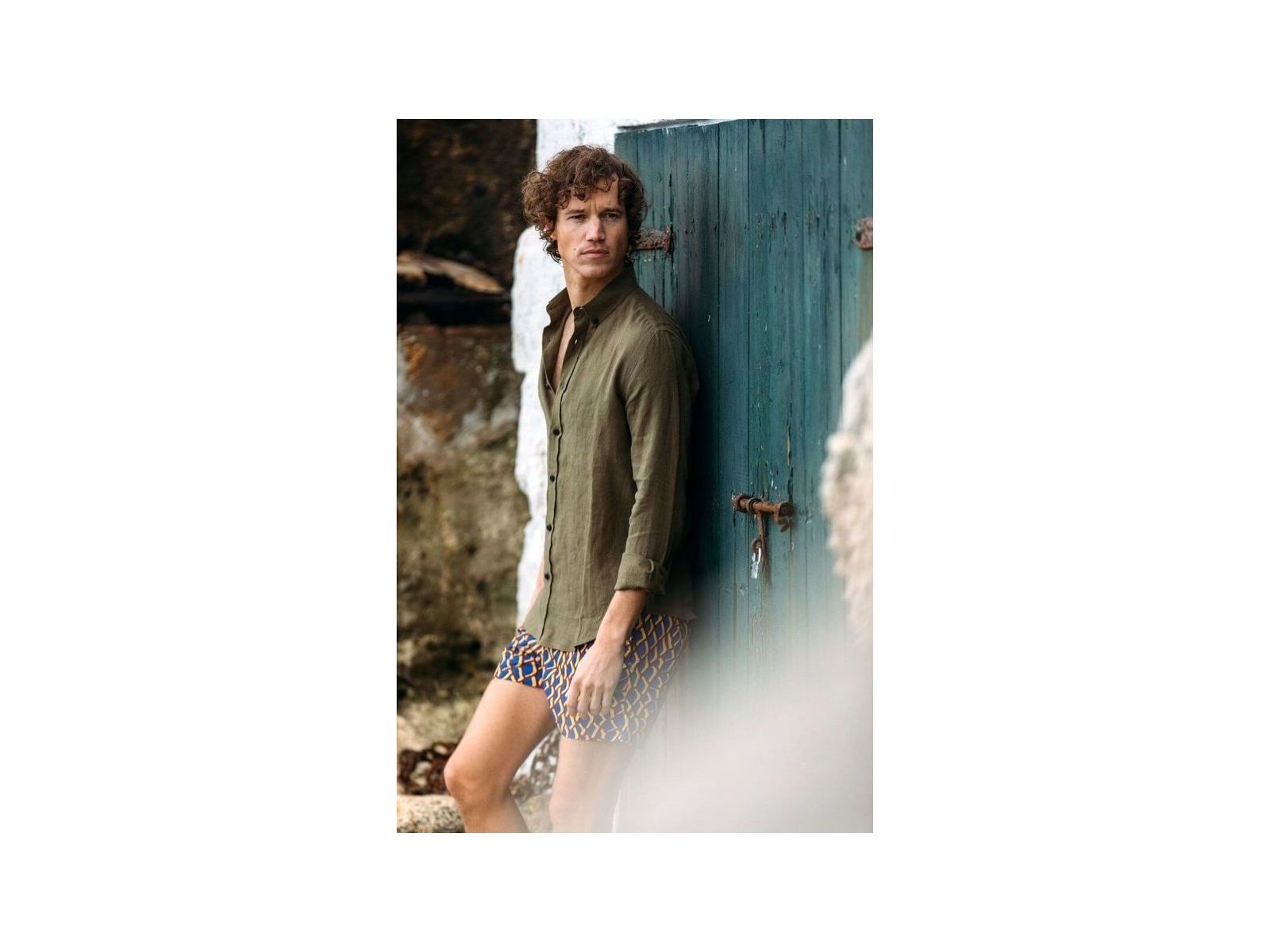 Homme portant une chemise en lin kaki, debout près d'une porte bleue, affichant un style décontracté.
