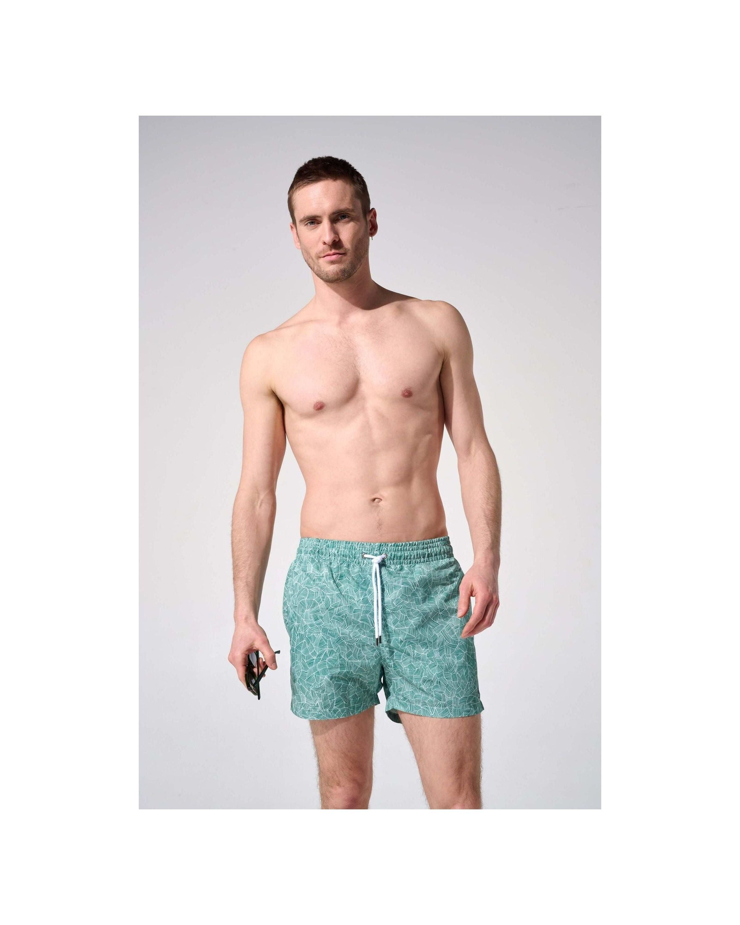 Homme portant des shorts de bain reflets, coupe ajustée, tissu recyclé, avec poches et ceinture élastique.
