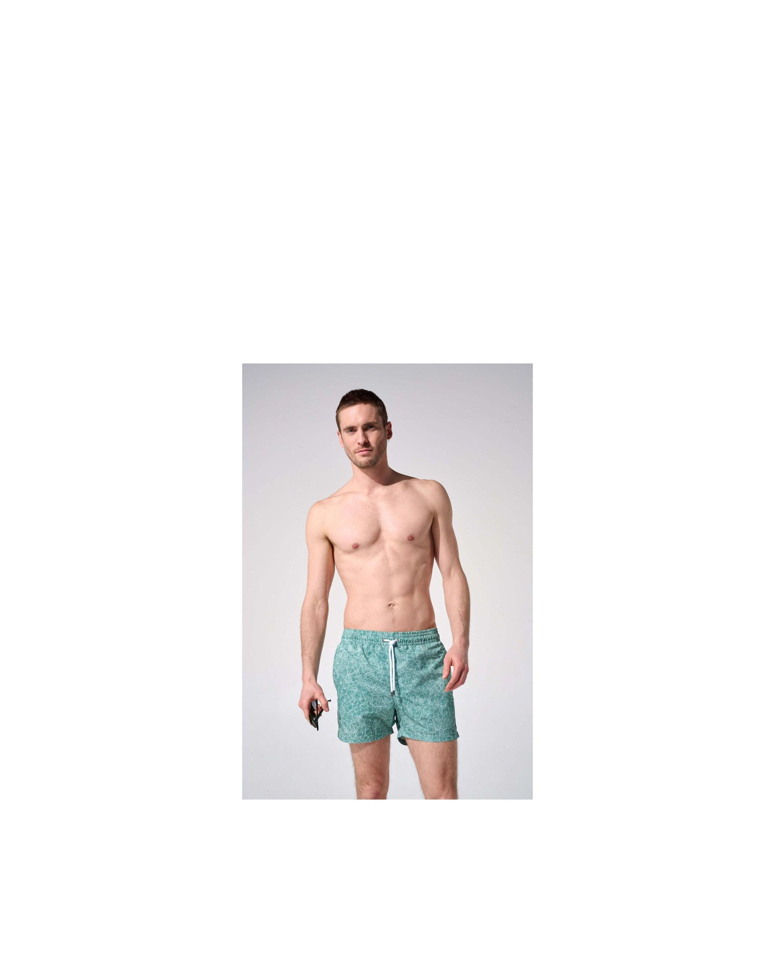 Homme portant des shorts de bain reflets, coupe ajustée, tissu recyclé, avec poches et ceinture élastique.