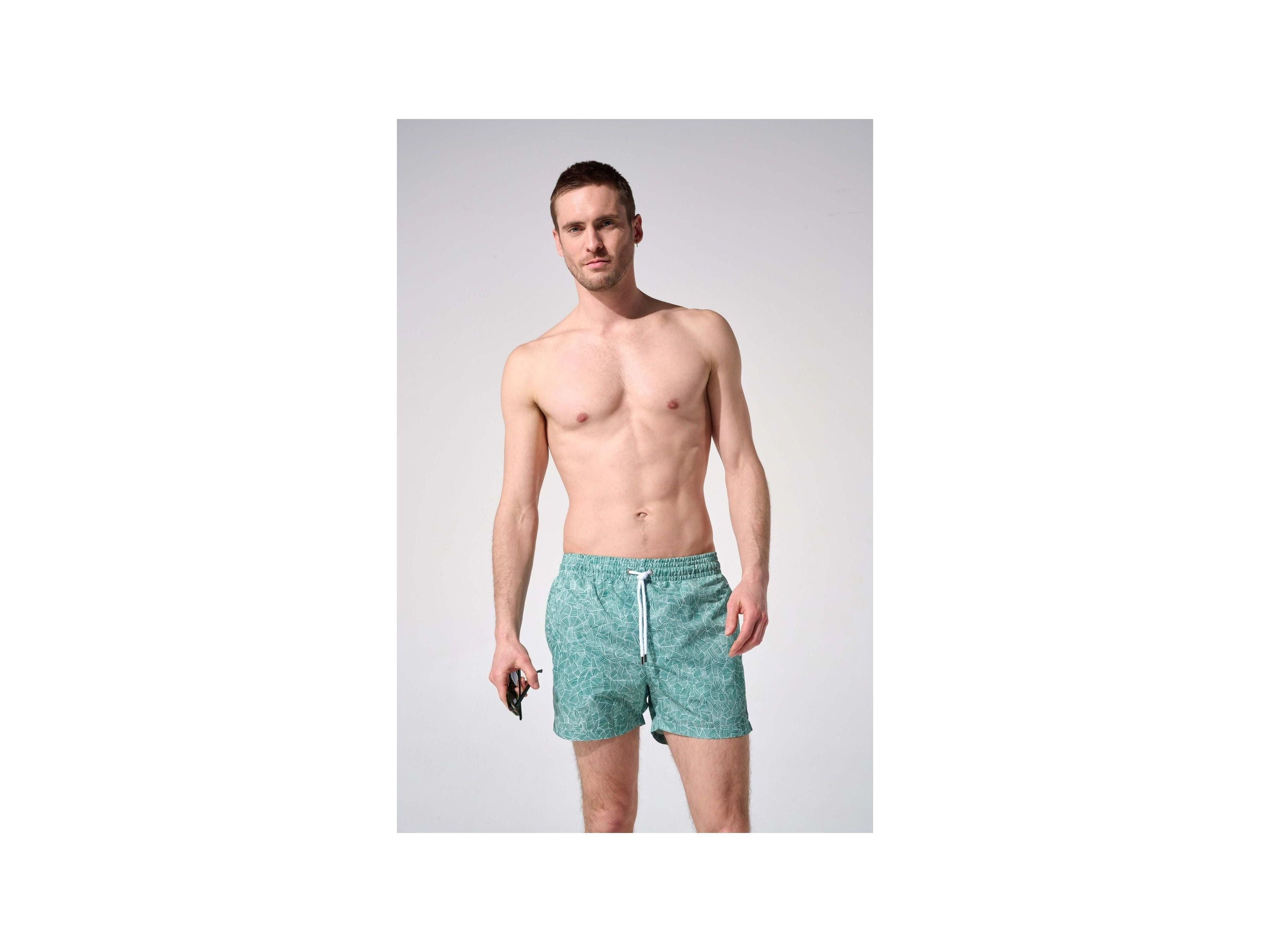 Homme portant des shorts de bain reflets, coupe ajustée, tissu recyclé, avec poches et ceinture élastique.
