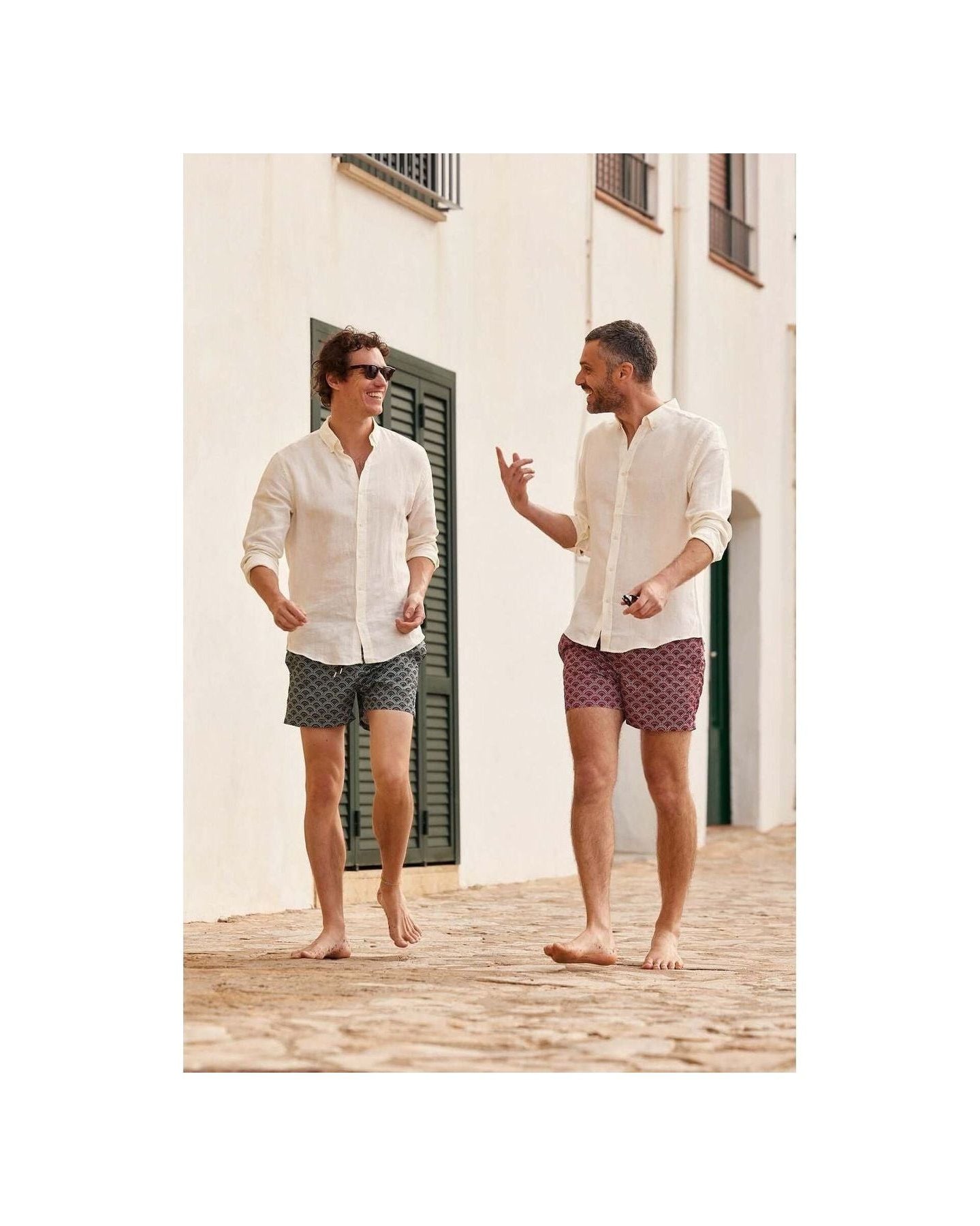 Two men wearing Ecume swim shorts, walking barefoot on a cobblestone path, enjoying a sunny day.