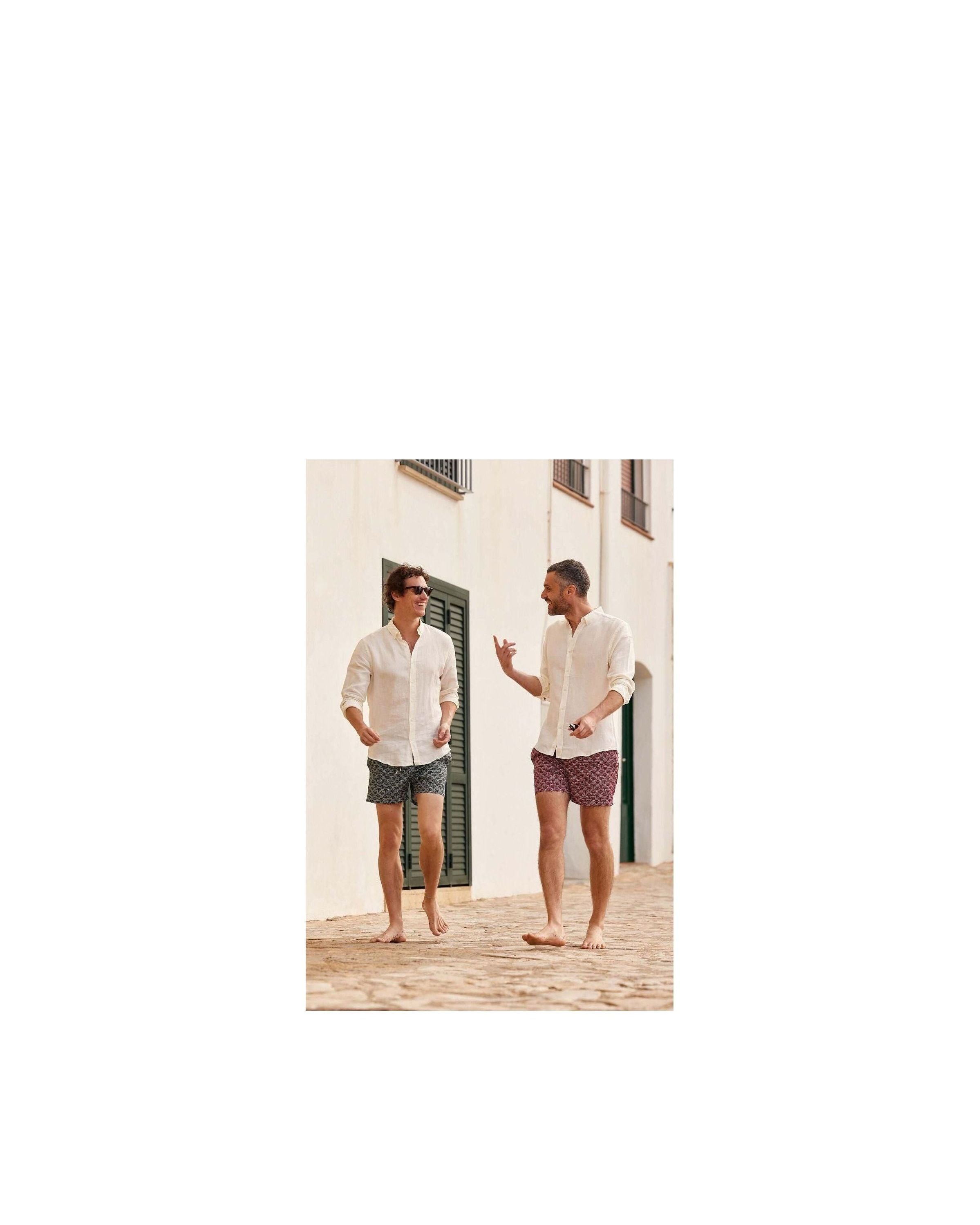 Two men wearing Ecume swim shorts, walking barefoot on a cobblestone path, enjoying a sunny day.