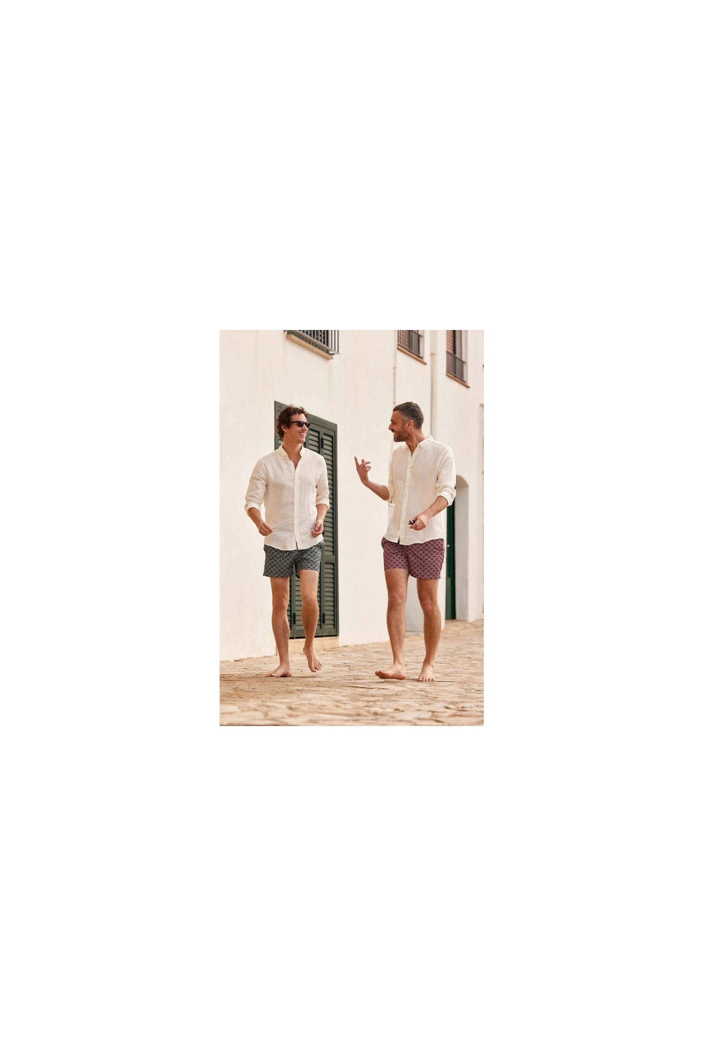Two men wearing Ecume swim shorts, walking barefoot on a cobblestone path, enjoying a sunny day.