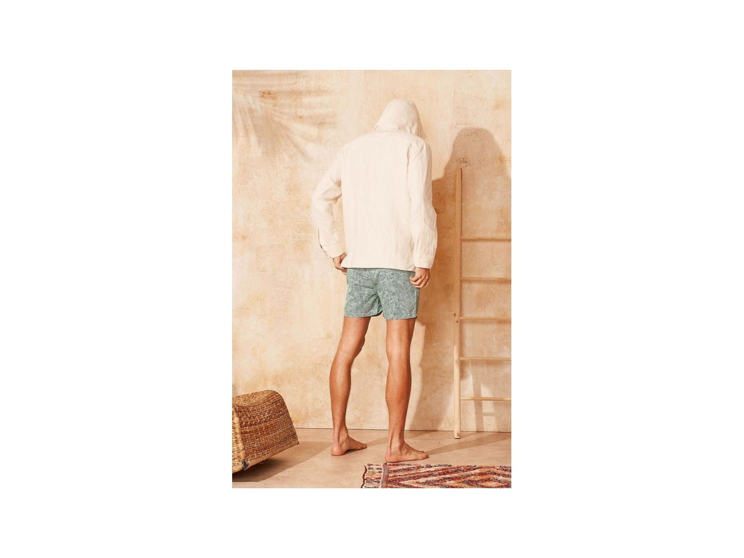 Homme vu de dos portant des shorts de bain Reflets en tissu recyclé, devant un mur beige, avec des pieds nus.