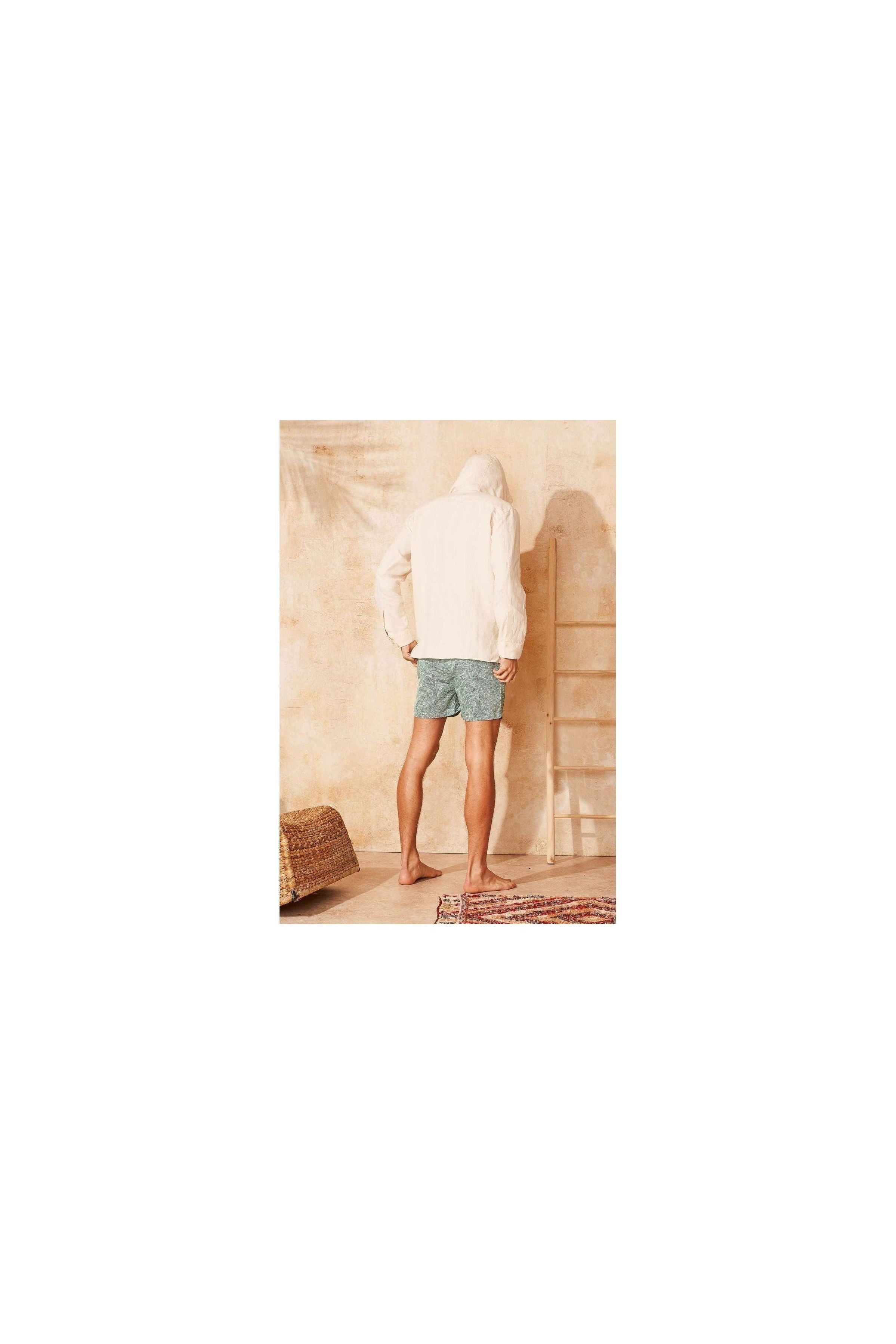 Homme vu de dos portant des shorts de bain Reflets en tissu recyclé, devant un mur beige, avec des pieds nus.