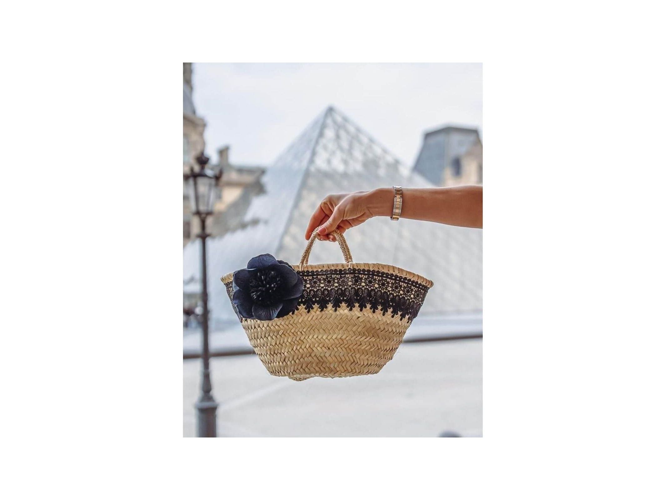 Petit panier noir élégant avec une rose noire, au pied de la pyramide du Louvre.
