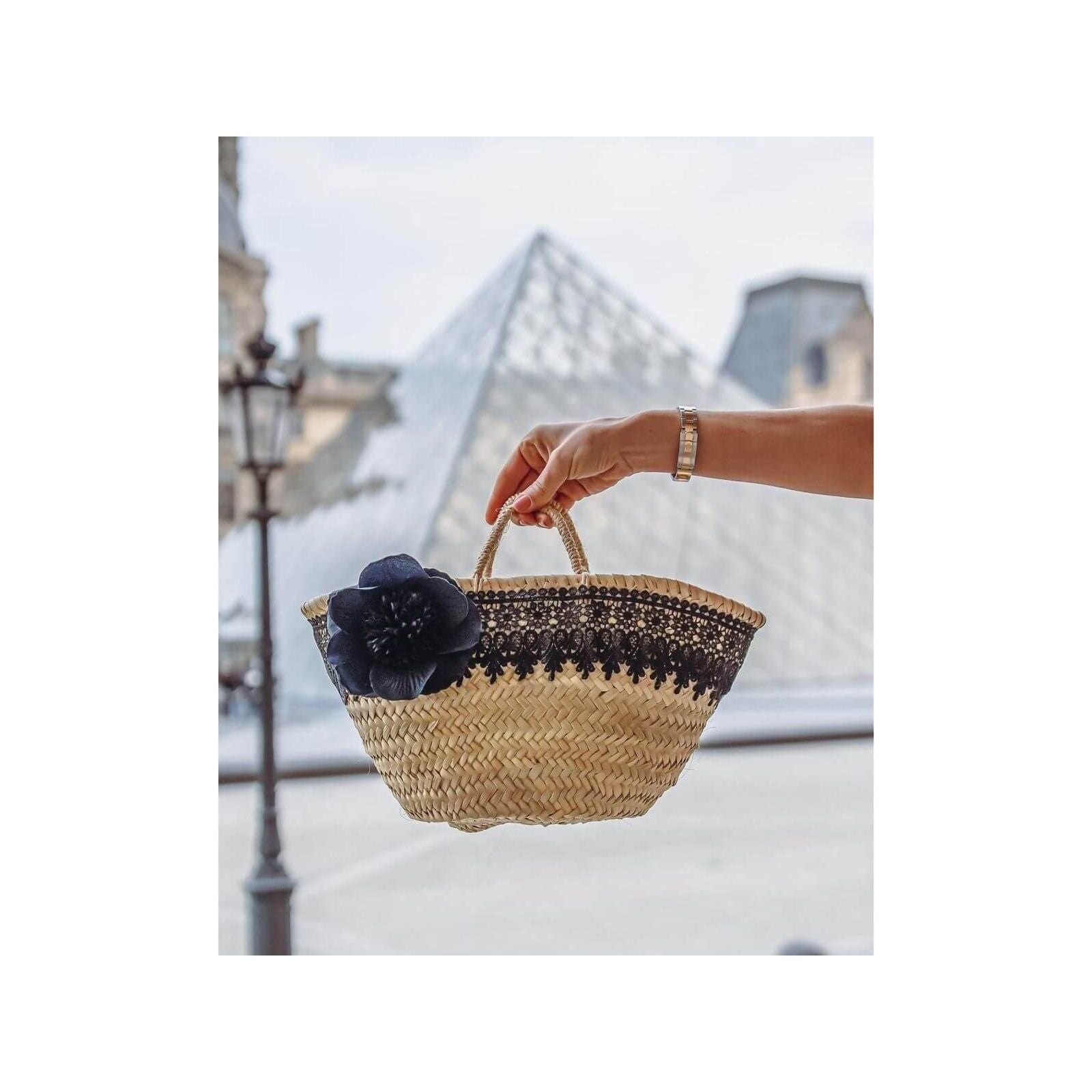 Petit panier noir élégant avec une rose noire, au pied de la pyramide du Louvre.