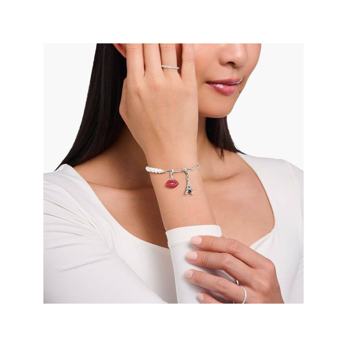 Bracelet charm featuring Eiffel Tower and red lips charm, worn elegantly by a woman.