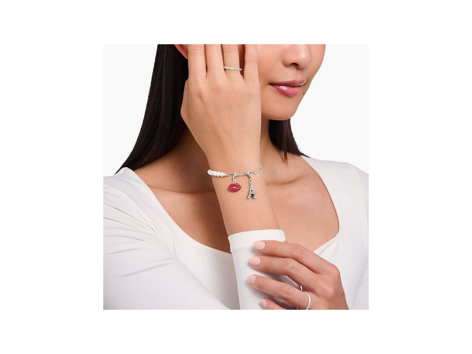 Bracelet charm featuring Eiffel Tower and red lips charm, worn elegantly by a woman.