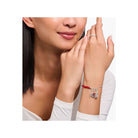 Femme portant un bracelet avec un charm en argent et une rose rouge émaillée, affichant élégance et style.