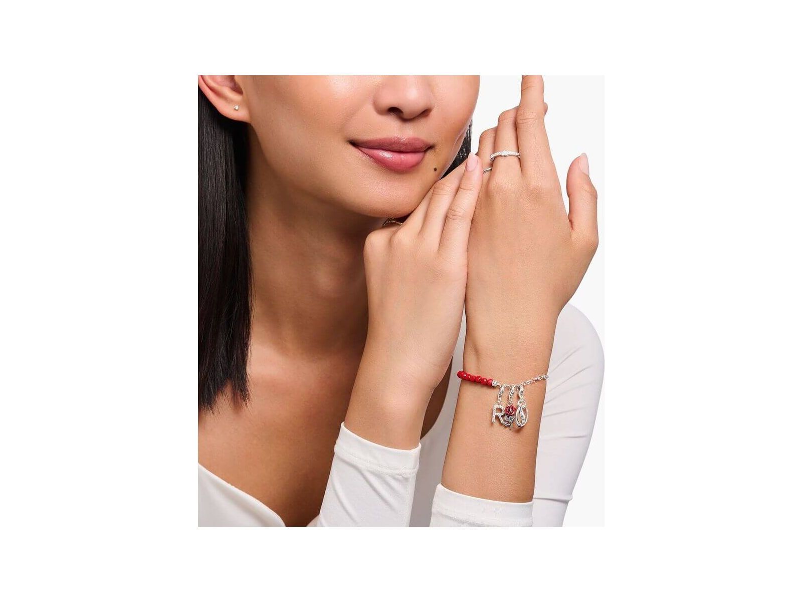 Femme portant un bracelet avec un charm en argent et une rose rouge émaillée, affichant élégance et style.
