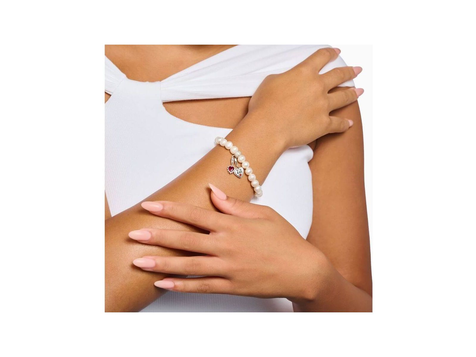 Femme portant un bracelet perle avec pendentif charm cœur en argent et saphir rouge, style élégant et raffiné.