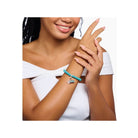 Femme souriante portant un bracelet charm avec perles turquoise et pendentif original en argent.