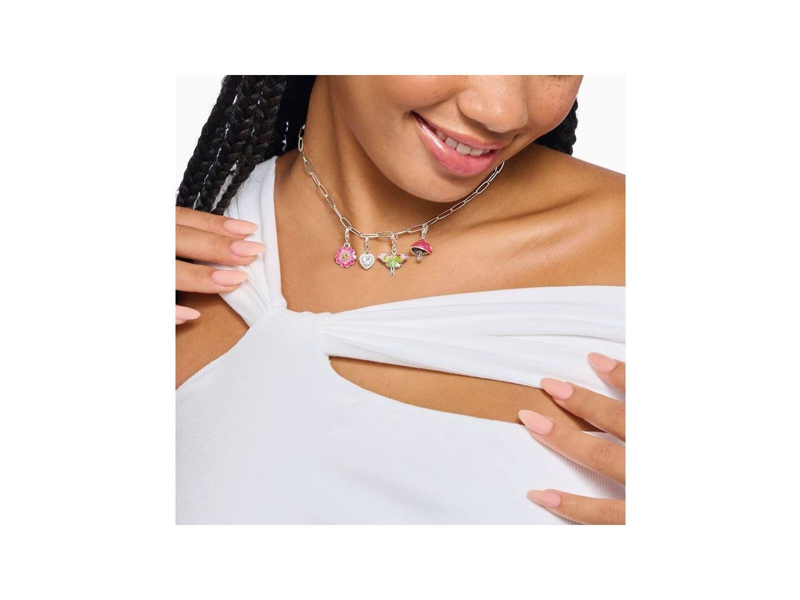 Femme souriante portant un collier en argent avec pendentifs champignon coloré et autres charms.