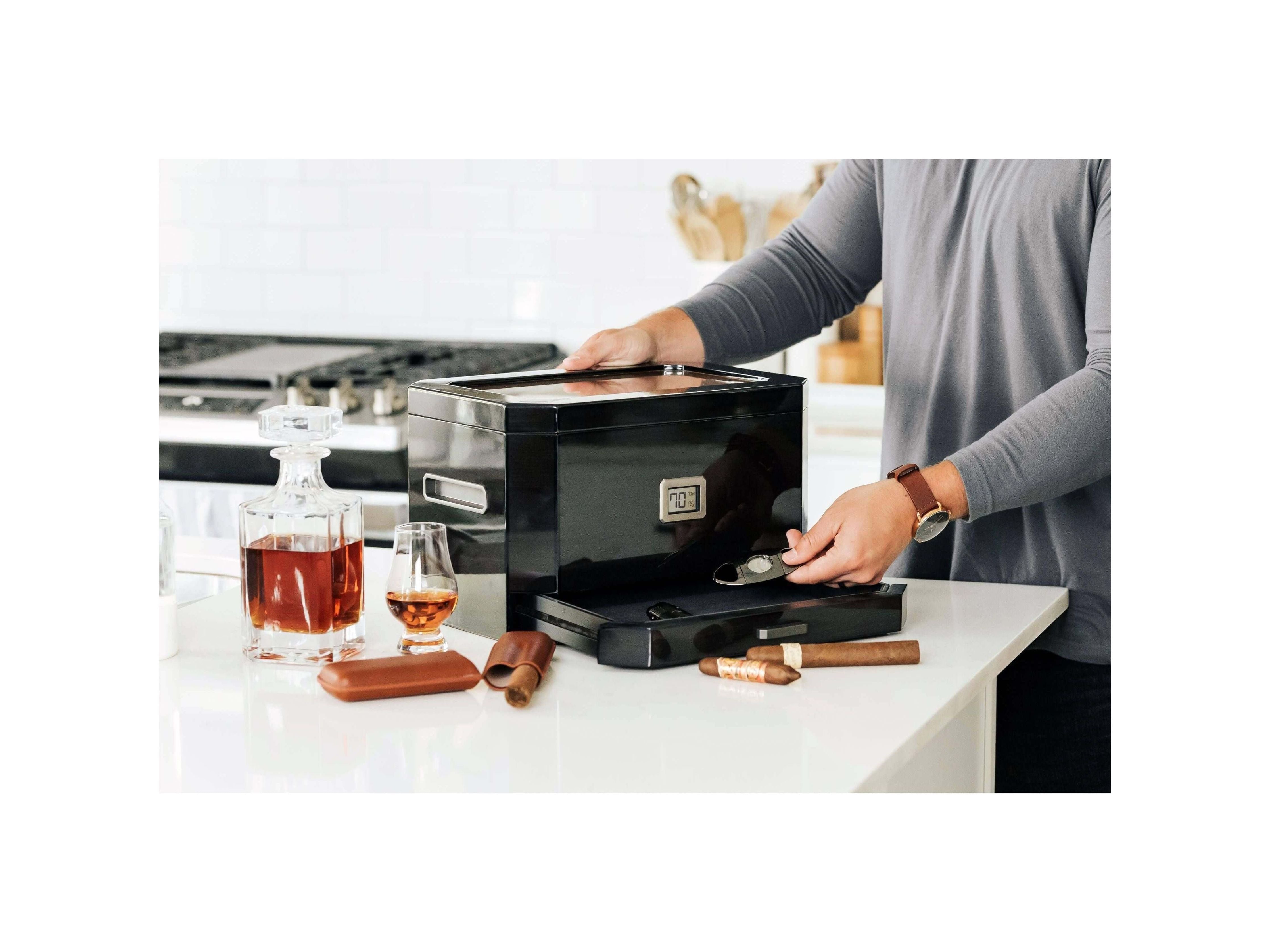 Homme utilisant un humidor à couvercle en verre Octodor dans une cuisine moderne avec des cigares et du whisky.