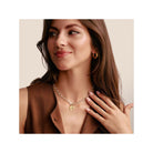 Femme portant un collier en argent avec un pendentif doré et des boucles d'oreilles en or, affichant un style élégant.