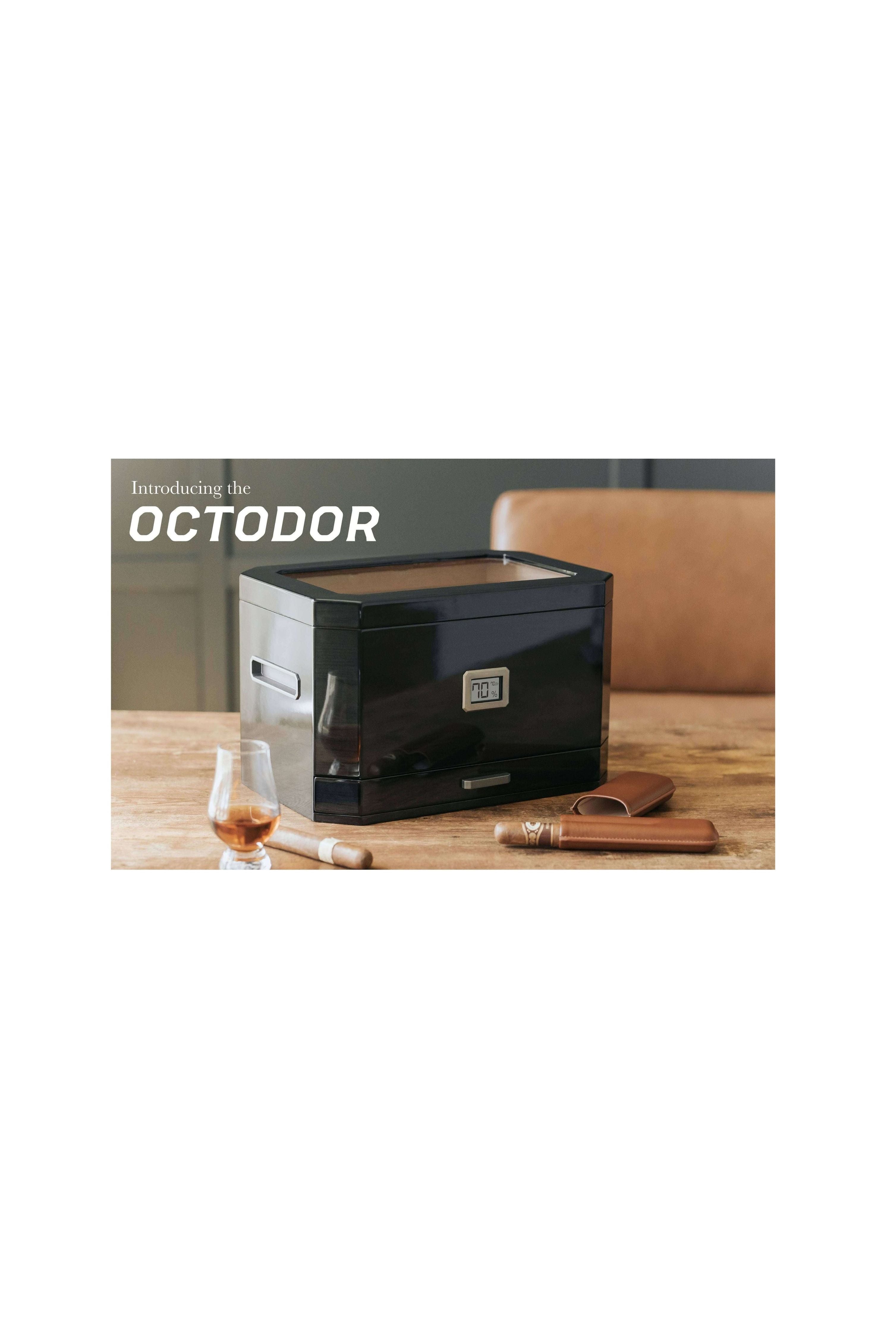 Humidor à couvercle en verre Octodor de Klaro sur une table, avec cigares et un verre de whisky.