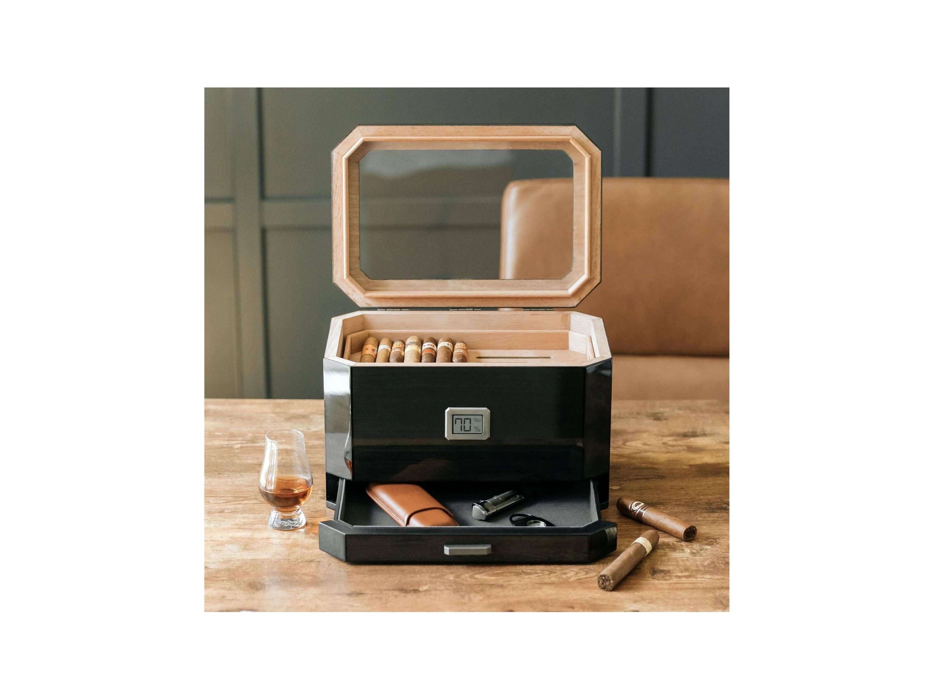 Humidor à couvercle en verre Octodor avec cigares, verre à whisky et accessoires sur une table en bois.