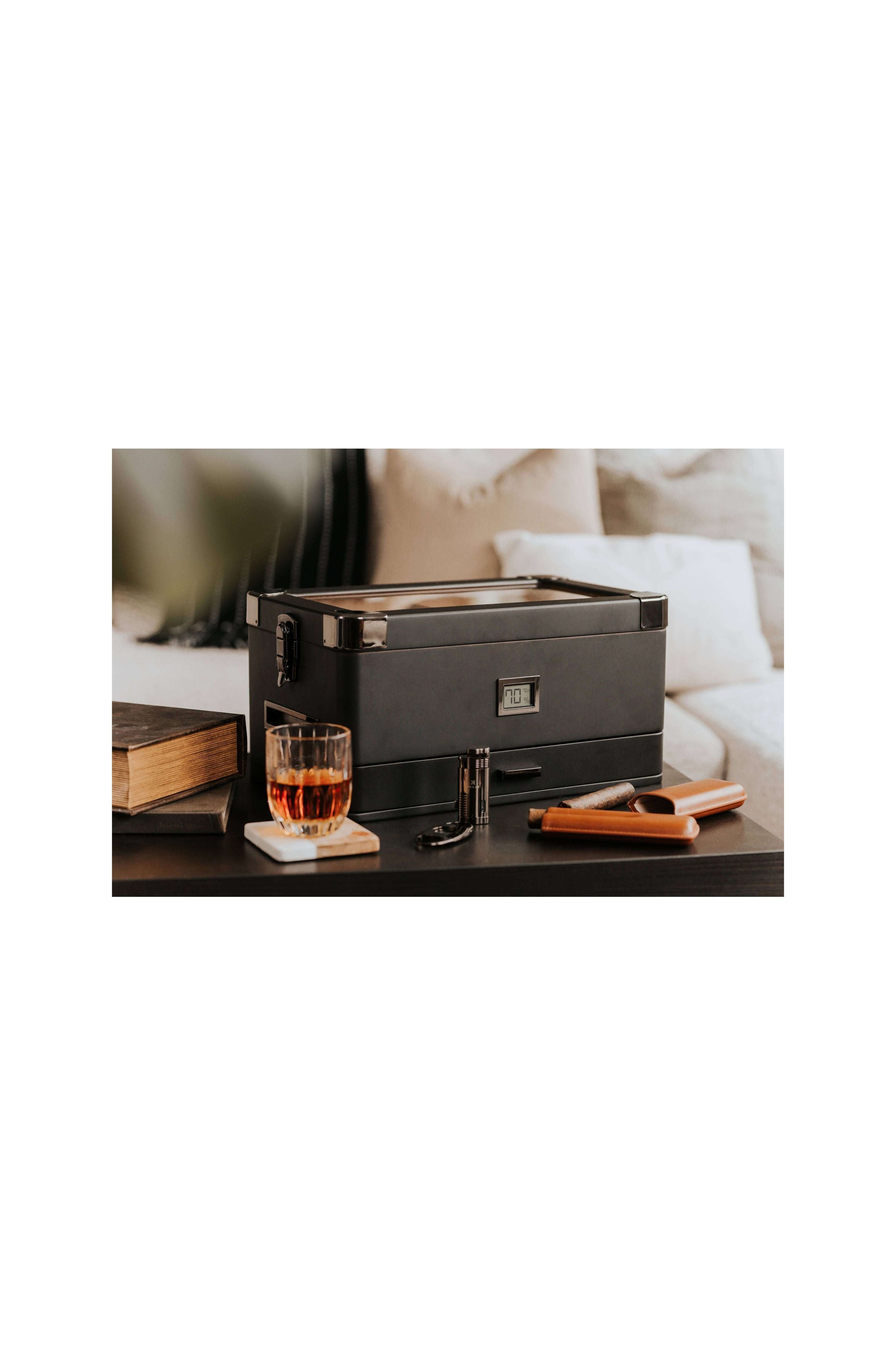 Humidor militaire Black Edition with black matte finish, next to a glass of whiskey and cigar accessories on a table.