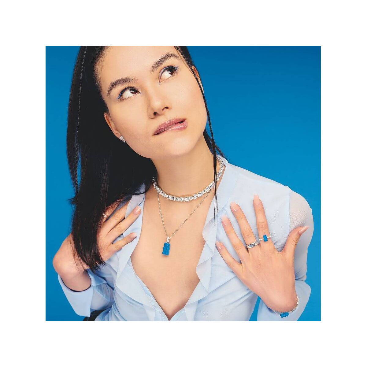 Modèle portant une chaîne à breloque Ours en argent et cristal bleu, avec accessoires assortis sur fond bleu.