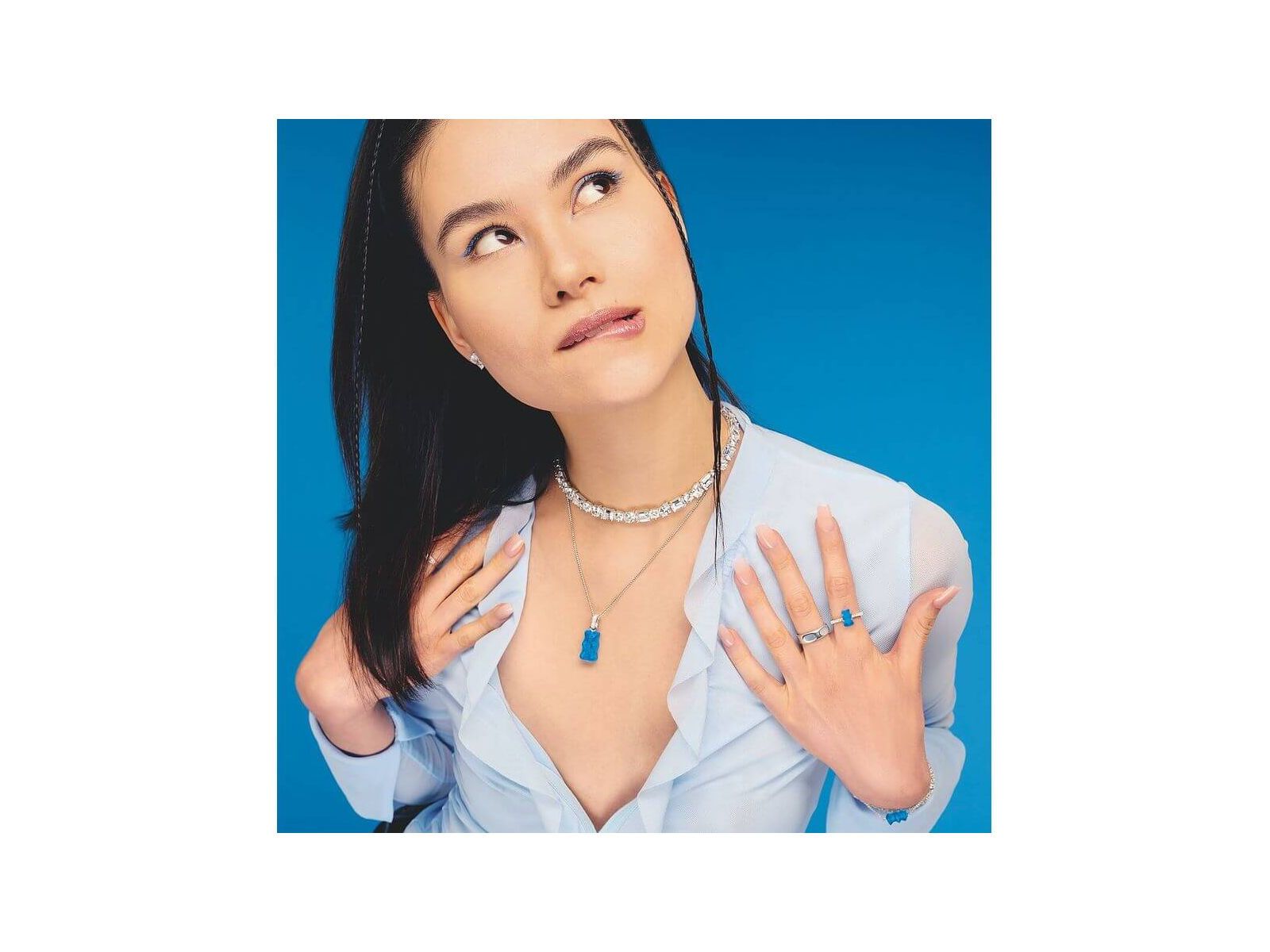 Modèle portant une chaîne à breloque Ours en argent et cristal bleu, avec accessoires assortis sur fond bleu.