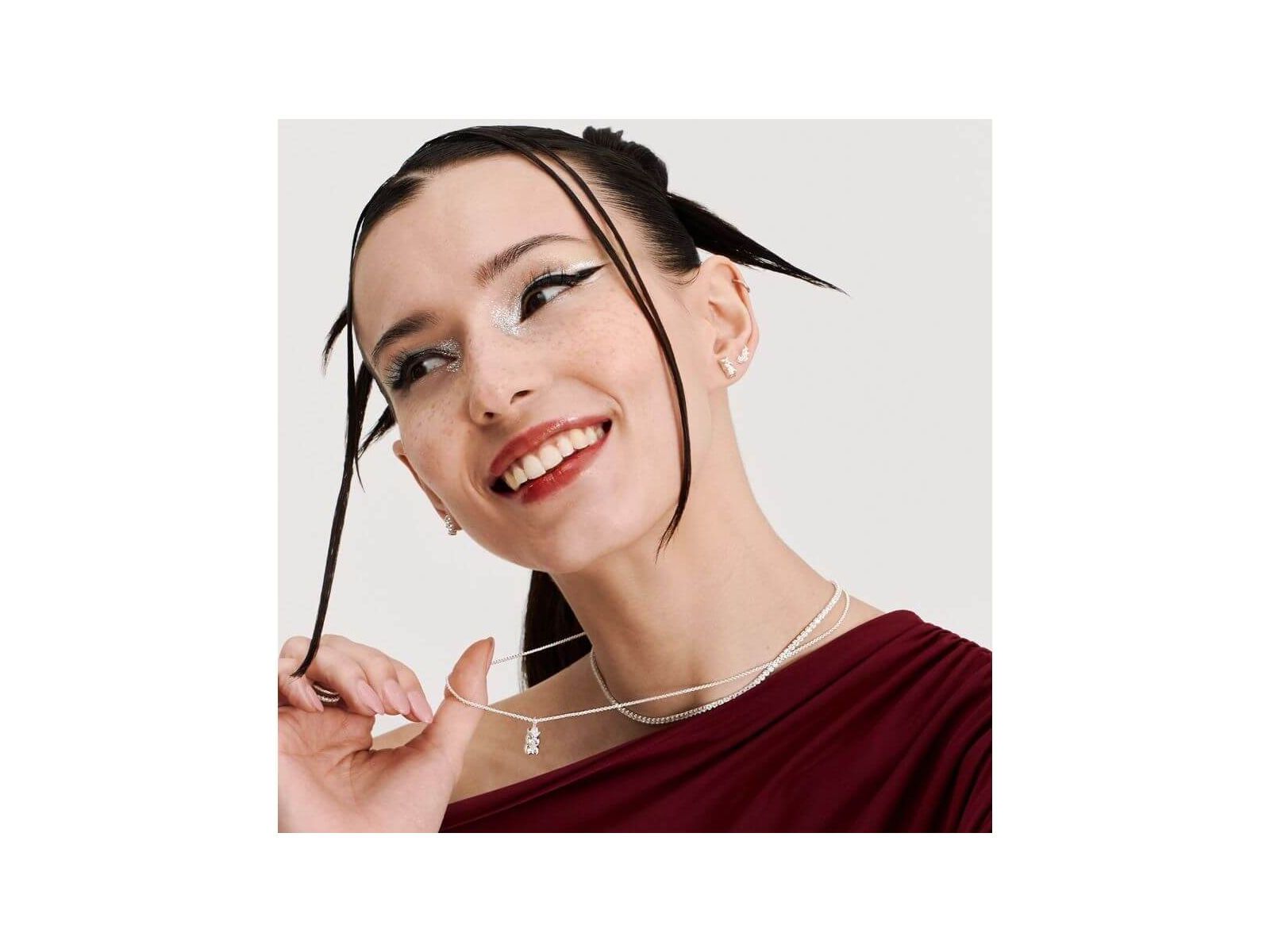 Model showcasing HARIBO silver bear earrings, smiling and wearing layered necklaces in a stylish outfit.