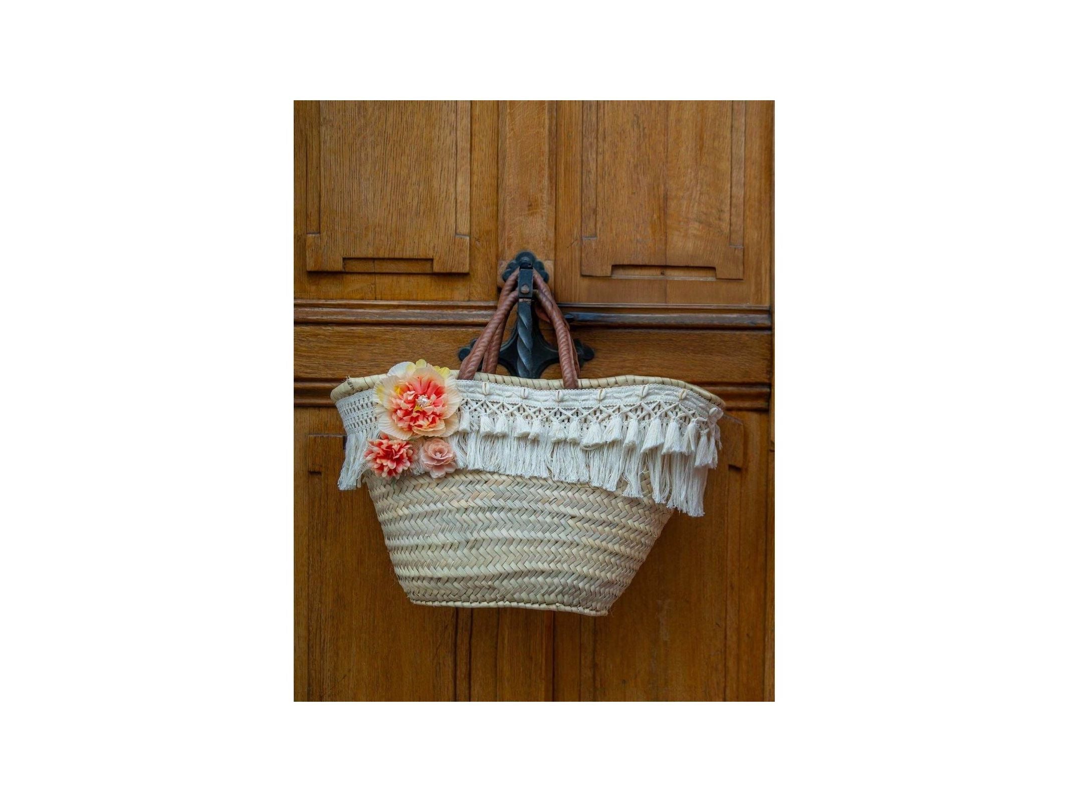 Stylish wicker basket adorned with white fringe and vibrant orange flowers, perfect for bohemian chic decor.