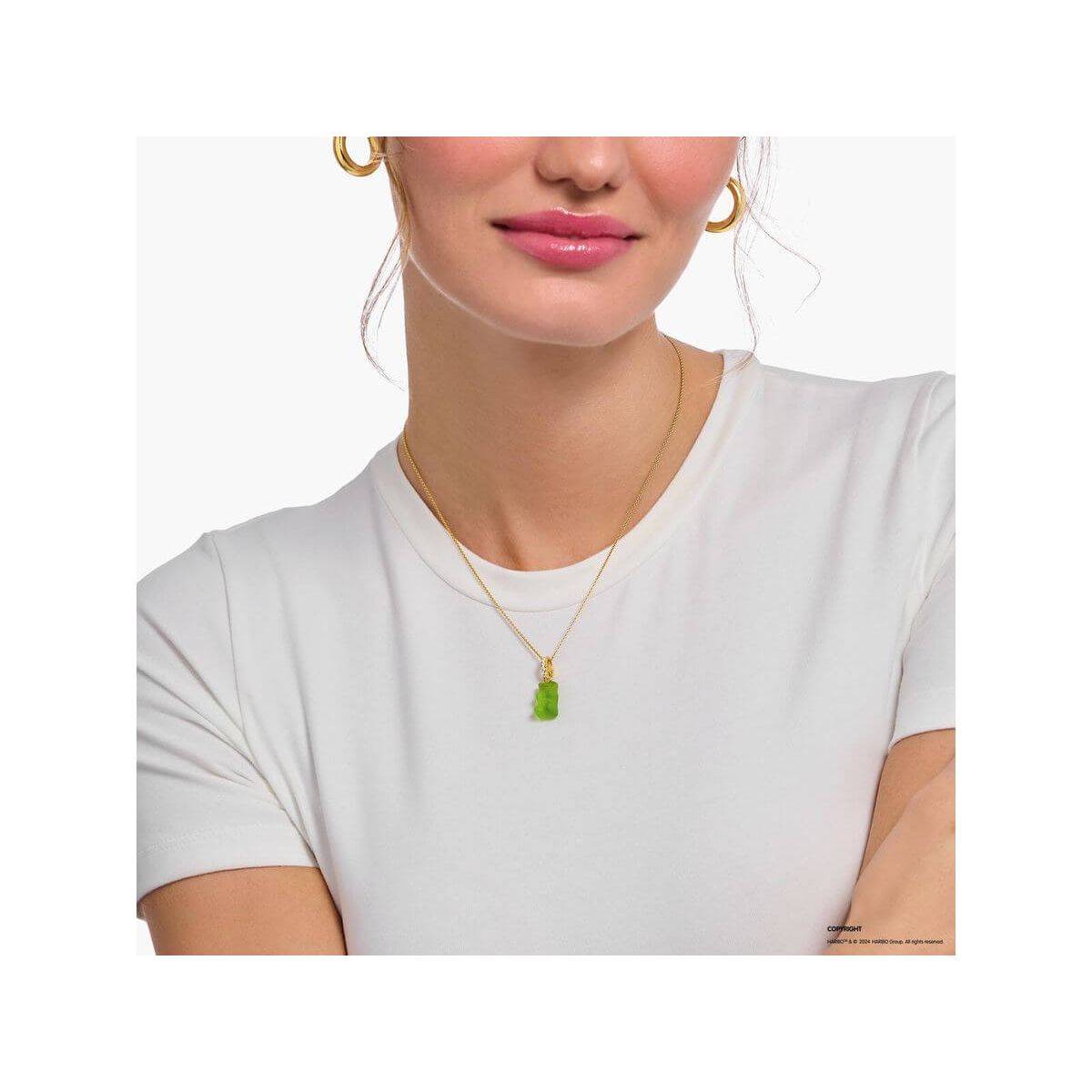 Gold chain necklace with green bear charm worn by a woman in a white shirt.