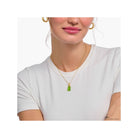 Gold chain necklace with green bear charm worn by a woman in a white shirt.