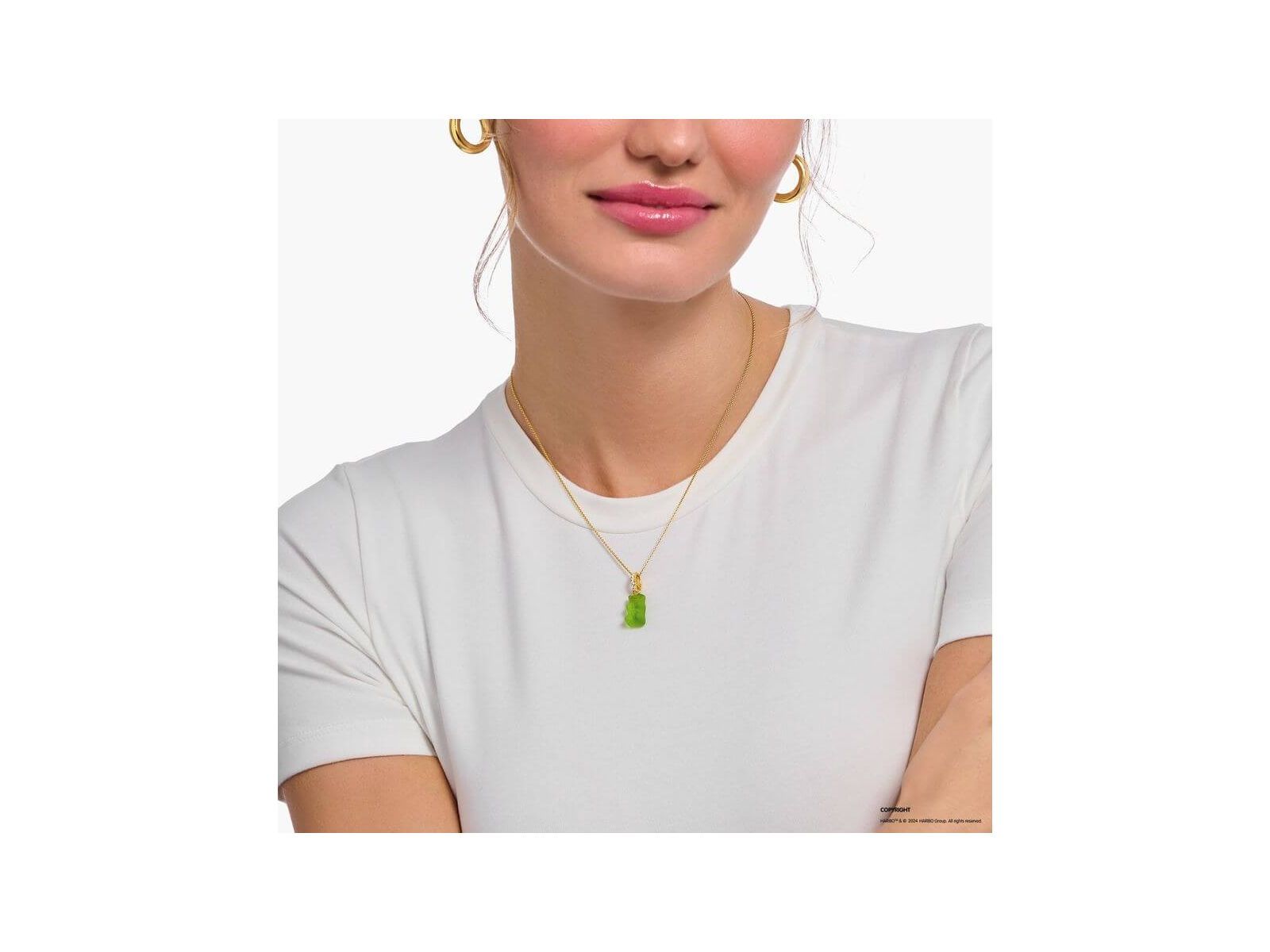 Gold chain necklace with green bear charm worn by a woman in a white shirt.