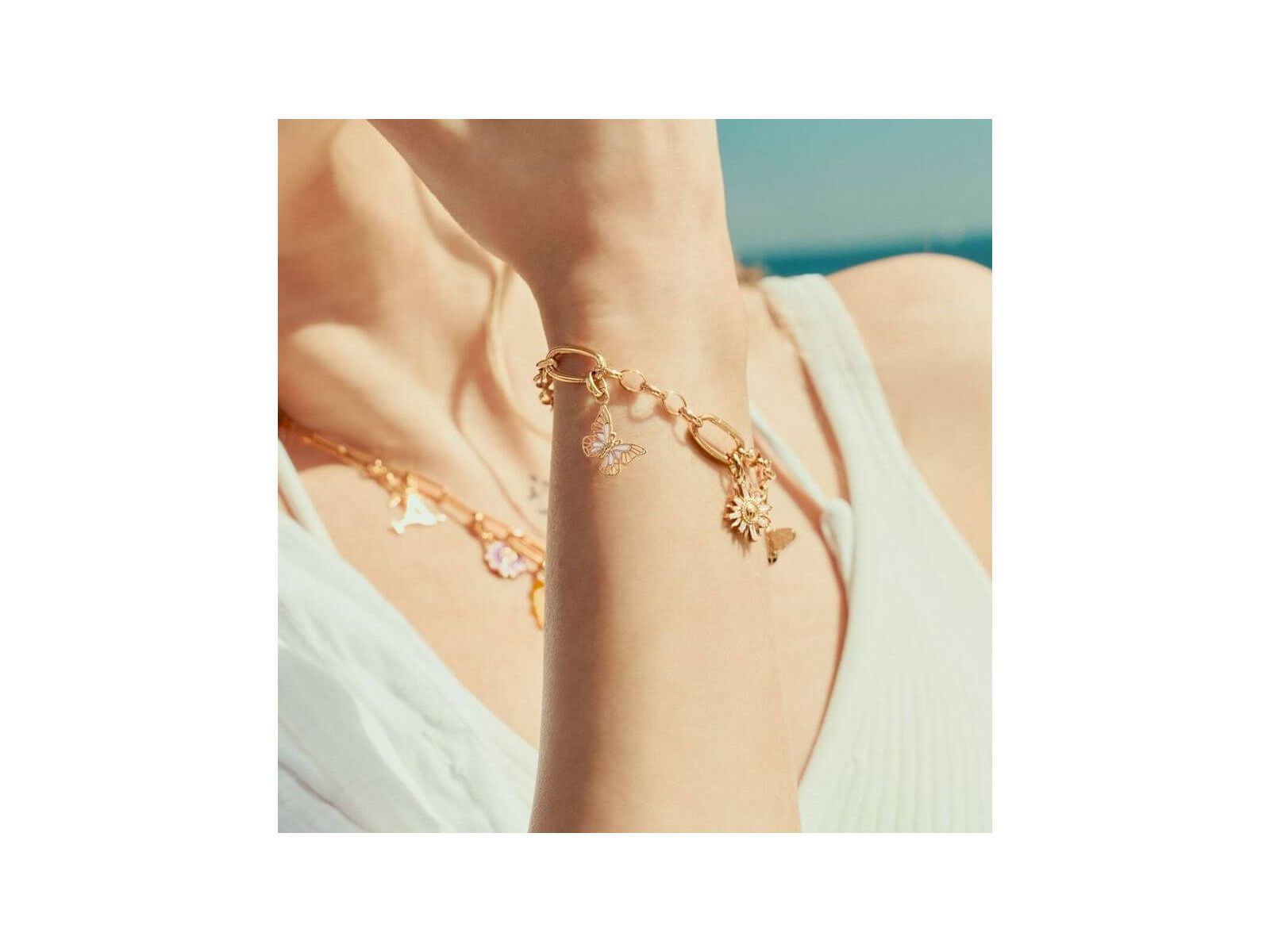 Pendentif charm papillon en plaqué or, porté sur bracelet délicat, capturant l'élégance estivale.